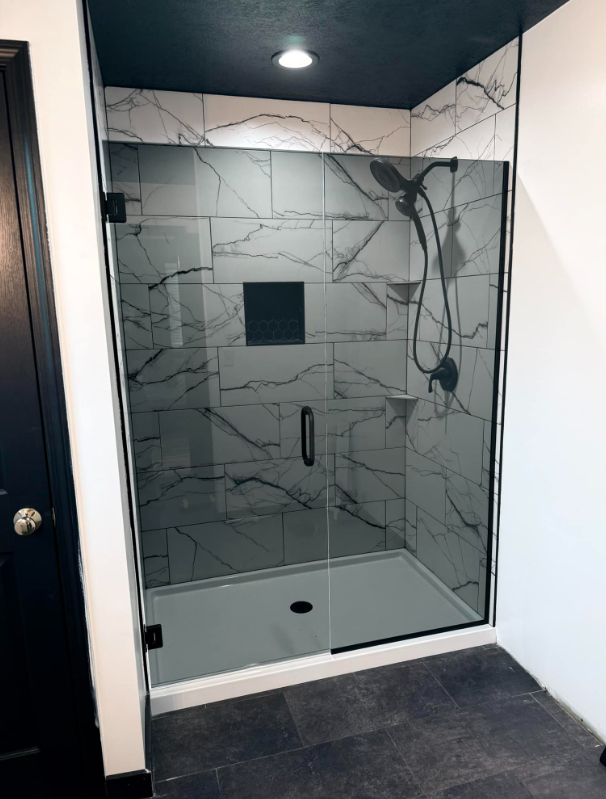 A bathroom with a walk in shower and a black door.