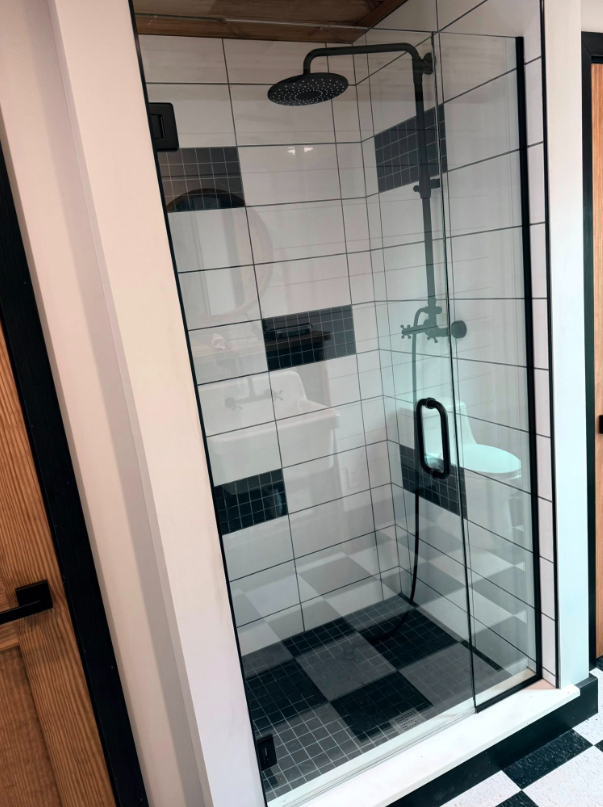 A bathroom with a walk in shower with a black and white checkered floor.