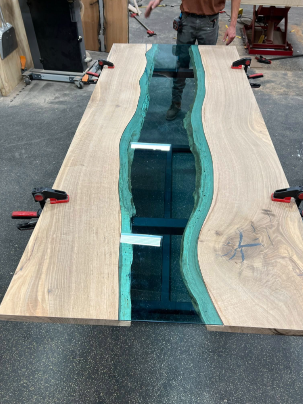 A man is standing next to a wooden table that looks like a river.