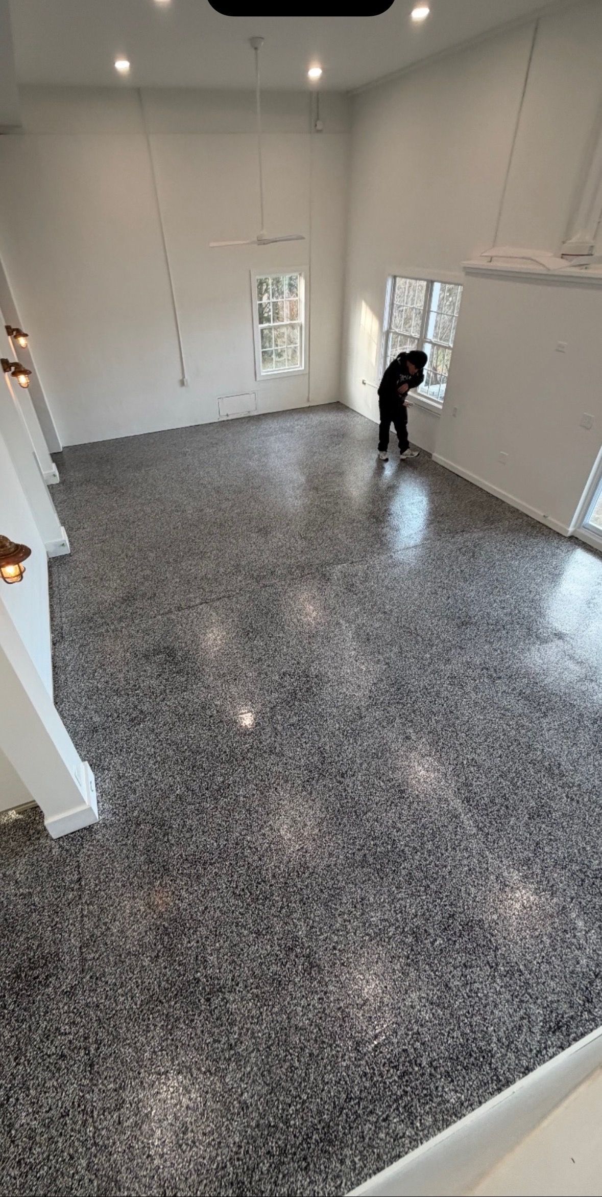 A wide-angle view of a large, high-ceilinged room with a glossy, grey granite-patterned floor and a person by a window.