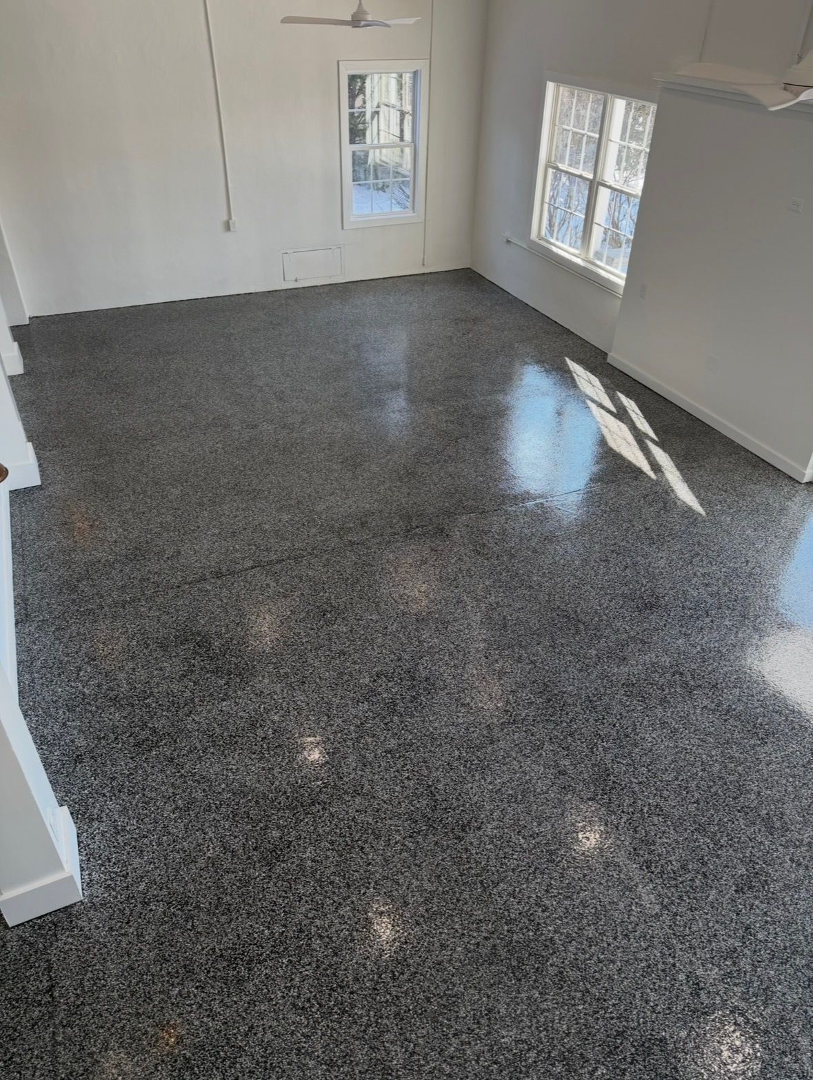 A room with a high-gloss, dark gray speckled epoxy floor, white walls, and two windows reflecting natural light.