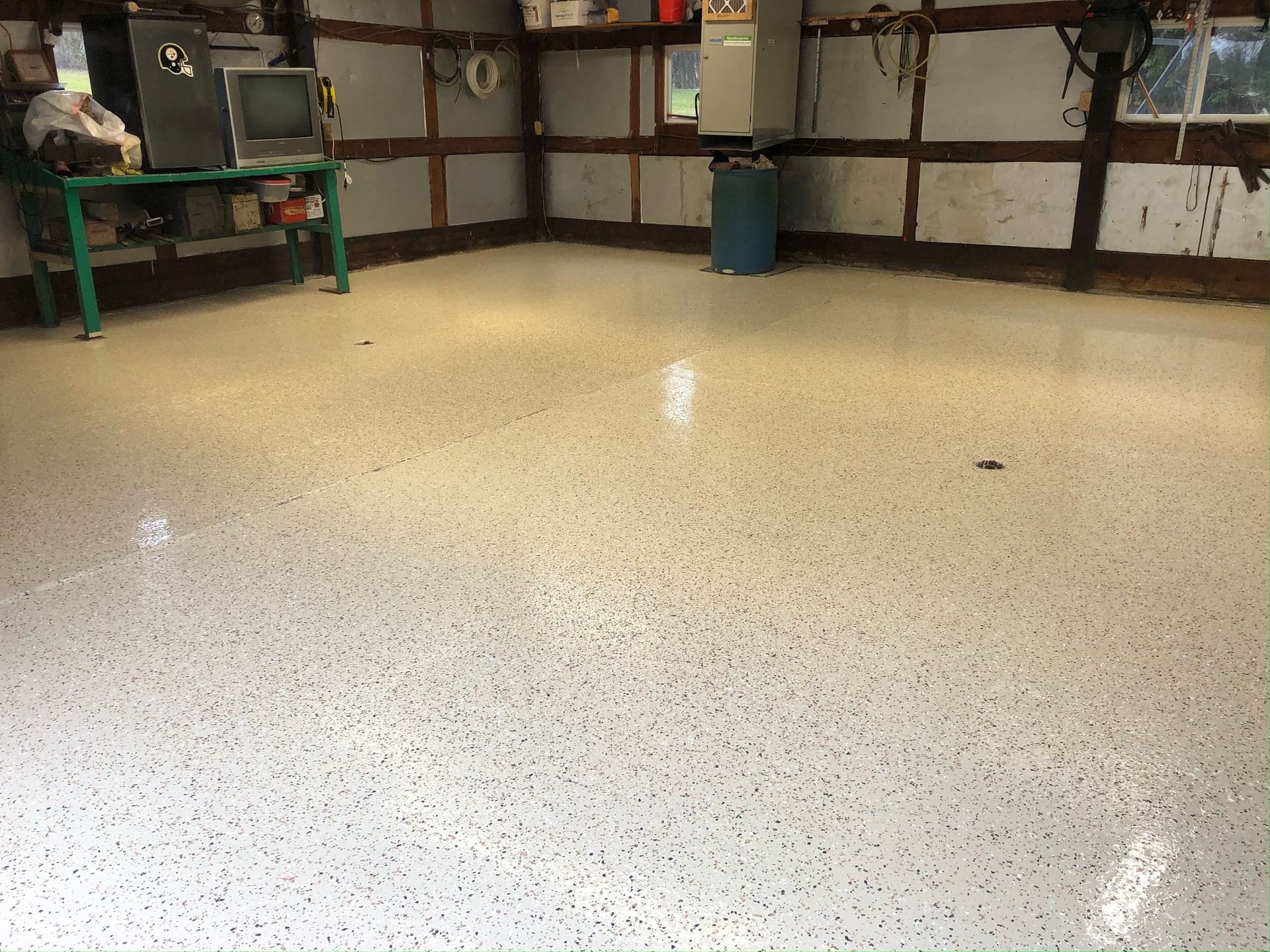 Garage with a light-colored, speckled epoxy floor finish and a workbench in the background.