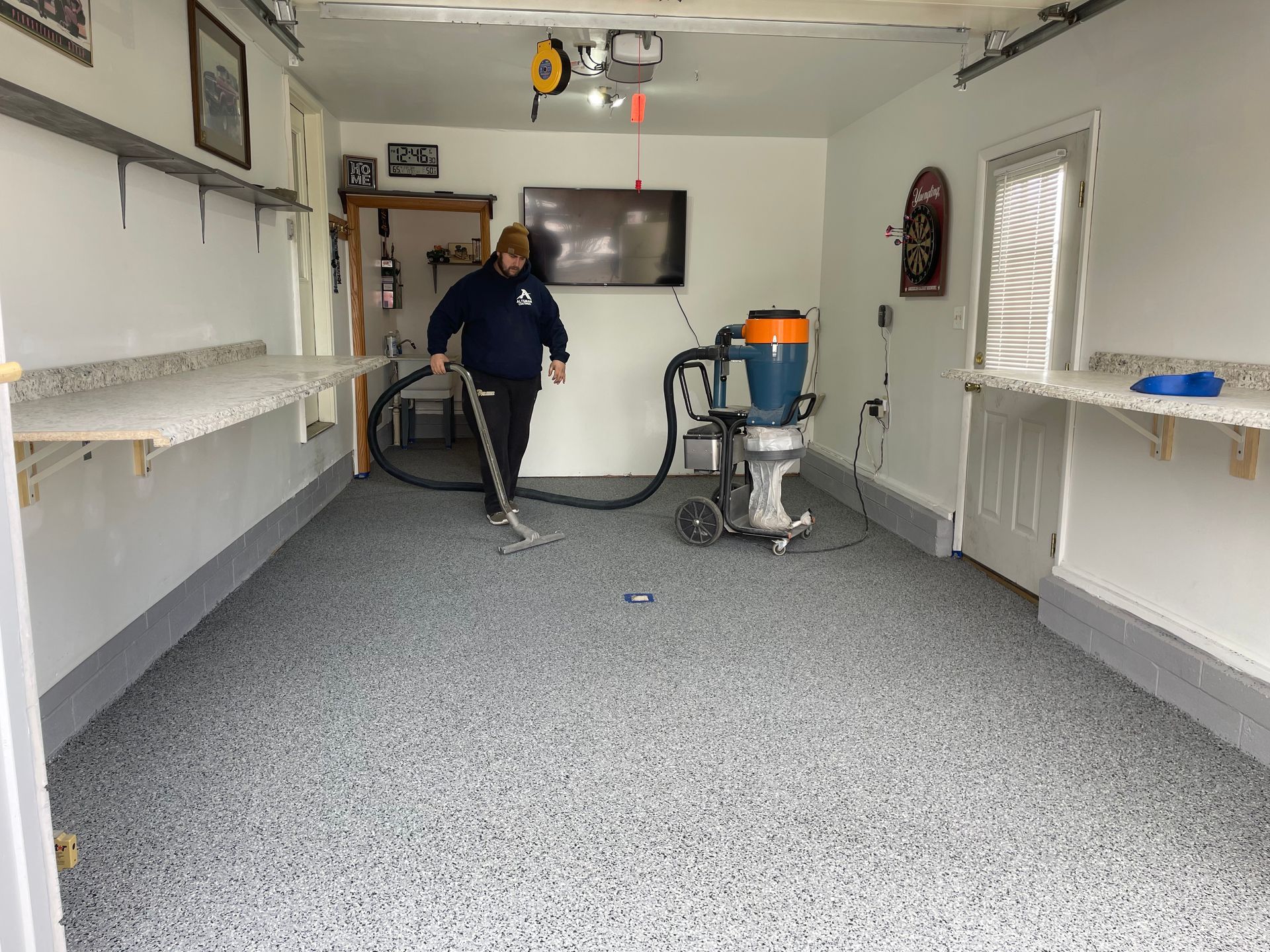 A person in a garage uses an industrial vacuum to clean a newly applied, gray speckled epoxy floor coating.