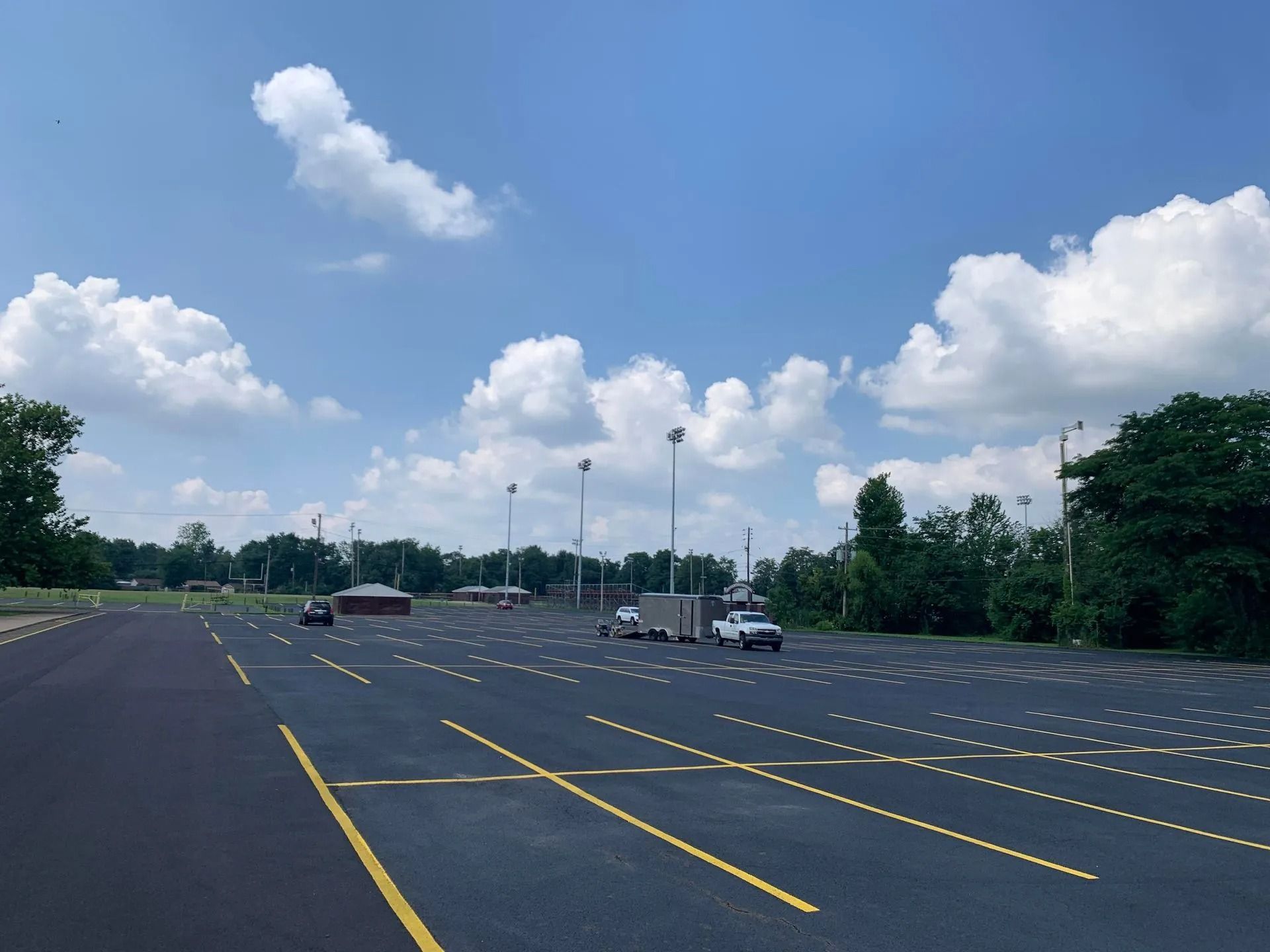 A paved parking lot with yellow lines and light poles under a blue sky with clouds.