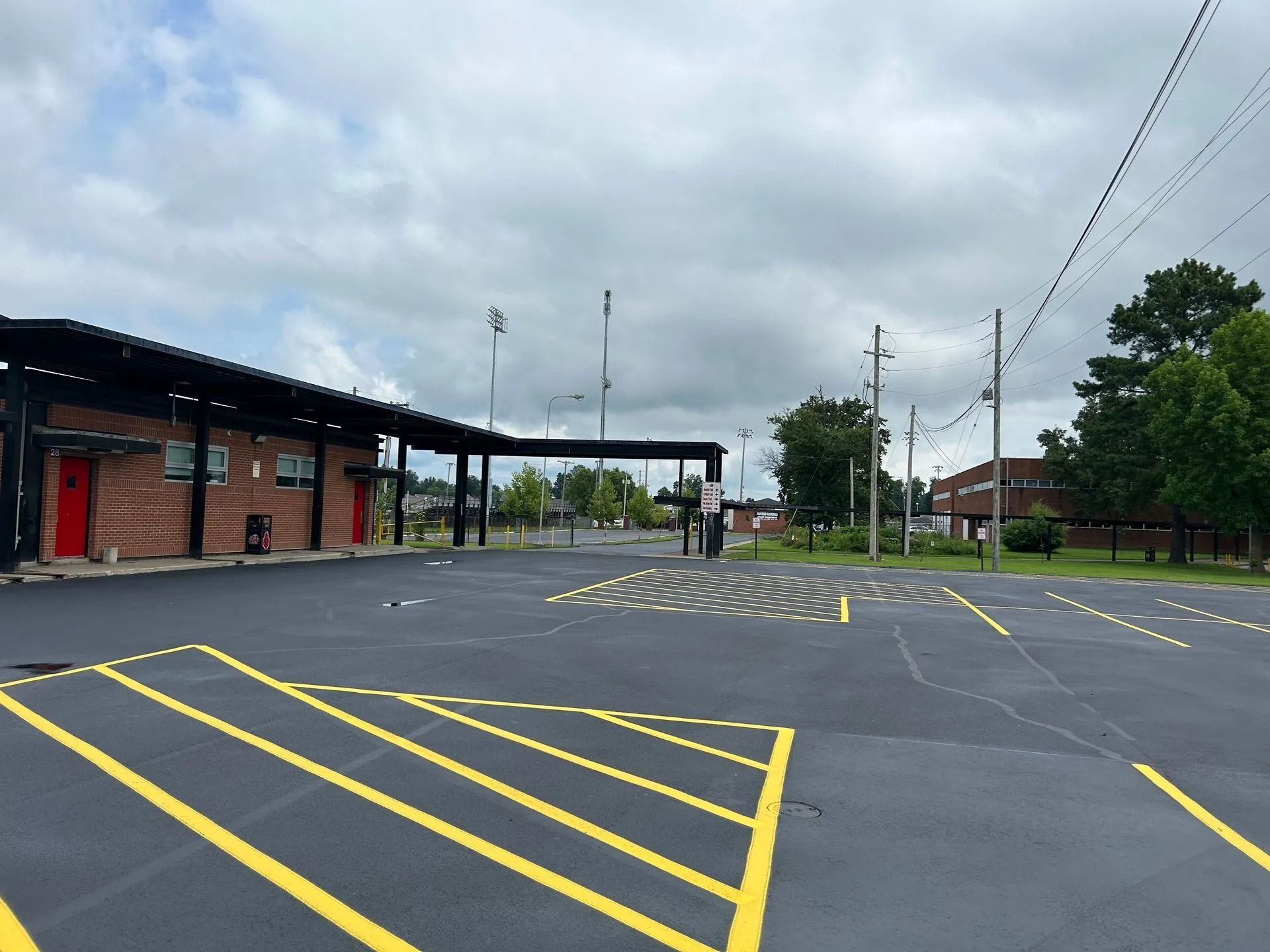 Black asphalt parking lot with yellow lines, a brick building with a black awning, and utility poles under a cloudy sky.