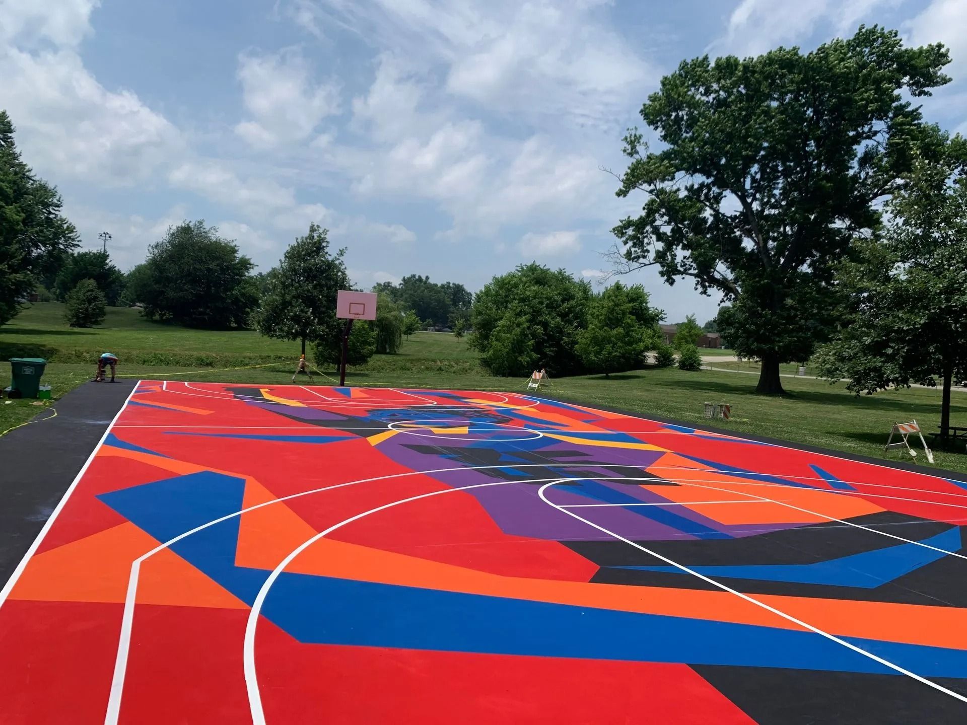 Colorful basketball court with a geometric design in a park, under a blue sky.