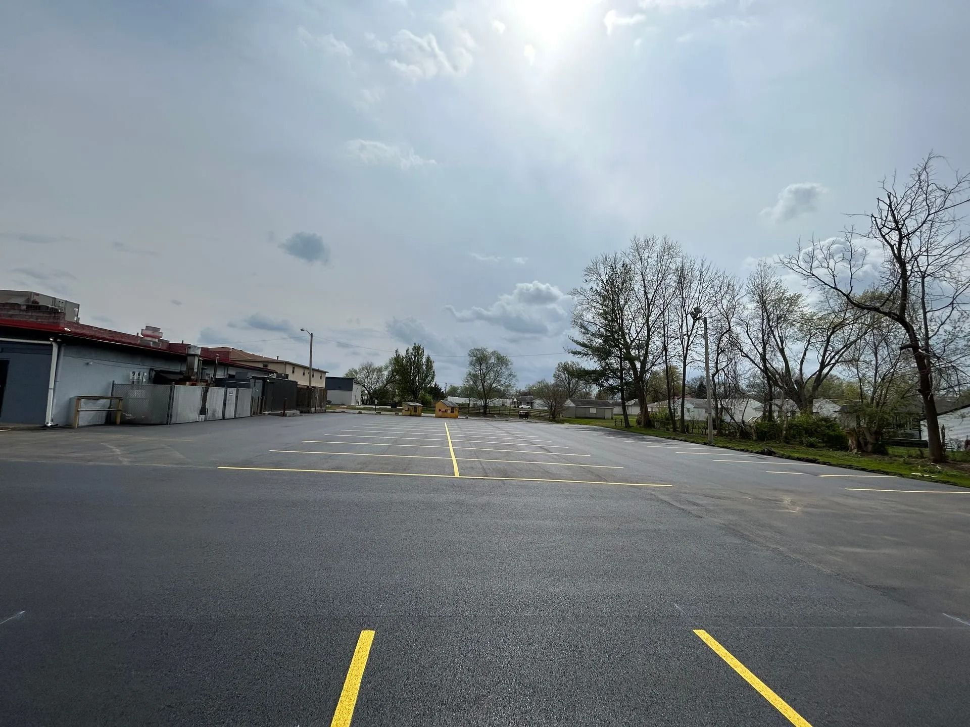 Empty asphalt parking lot with painted yellow lines and dots, cloudy sky above.