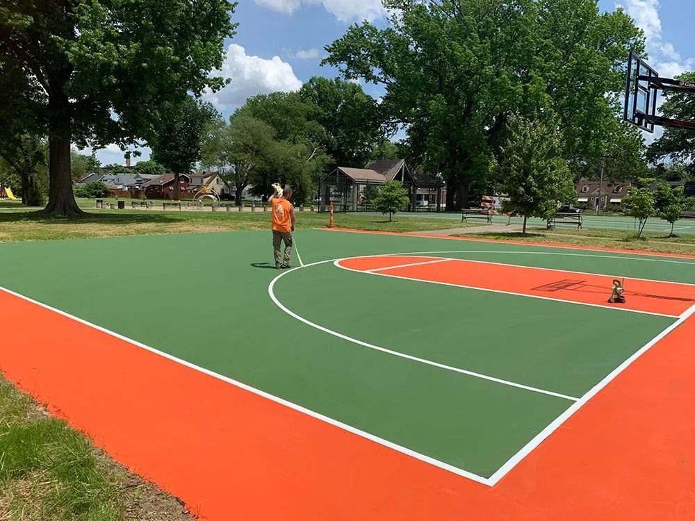 Basketball court with green and orange paint; person painting lines.