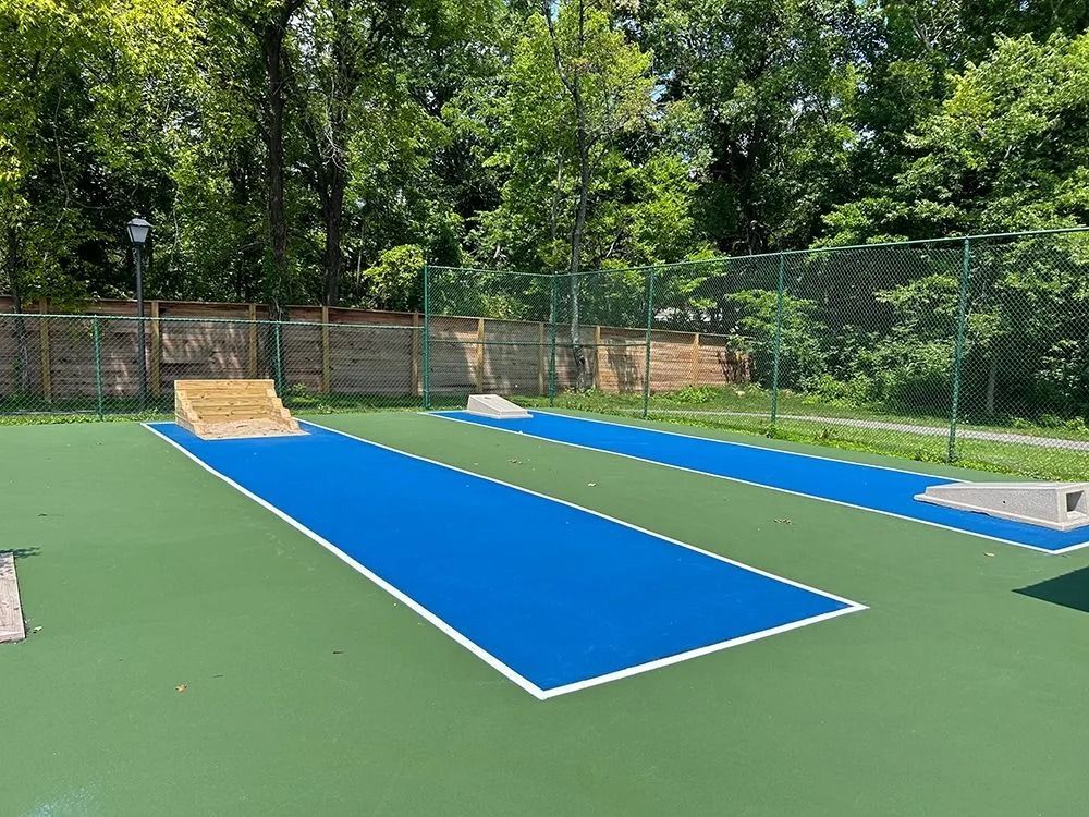 Outdoor shuffleboard court with blue playing surfaces and green surrounding area.