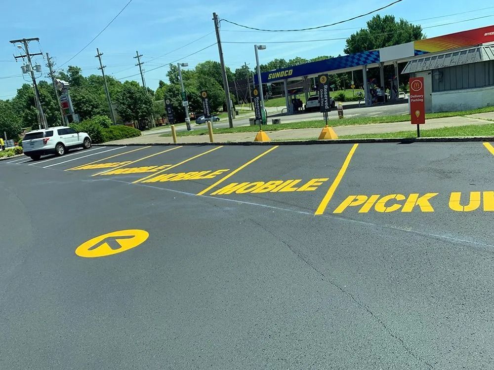 Asphalt parking lot with yellow painted "Mobile Pick Up" spaces and an arrow directing traffic. A gas station is in the background.