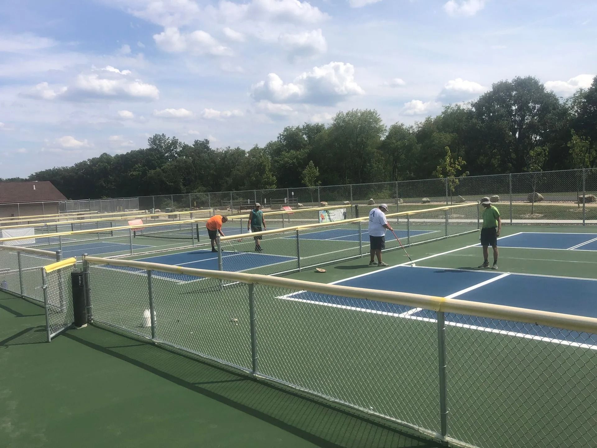 People playing pickleball on outdoor courts. Blue and green courts, sunny day.