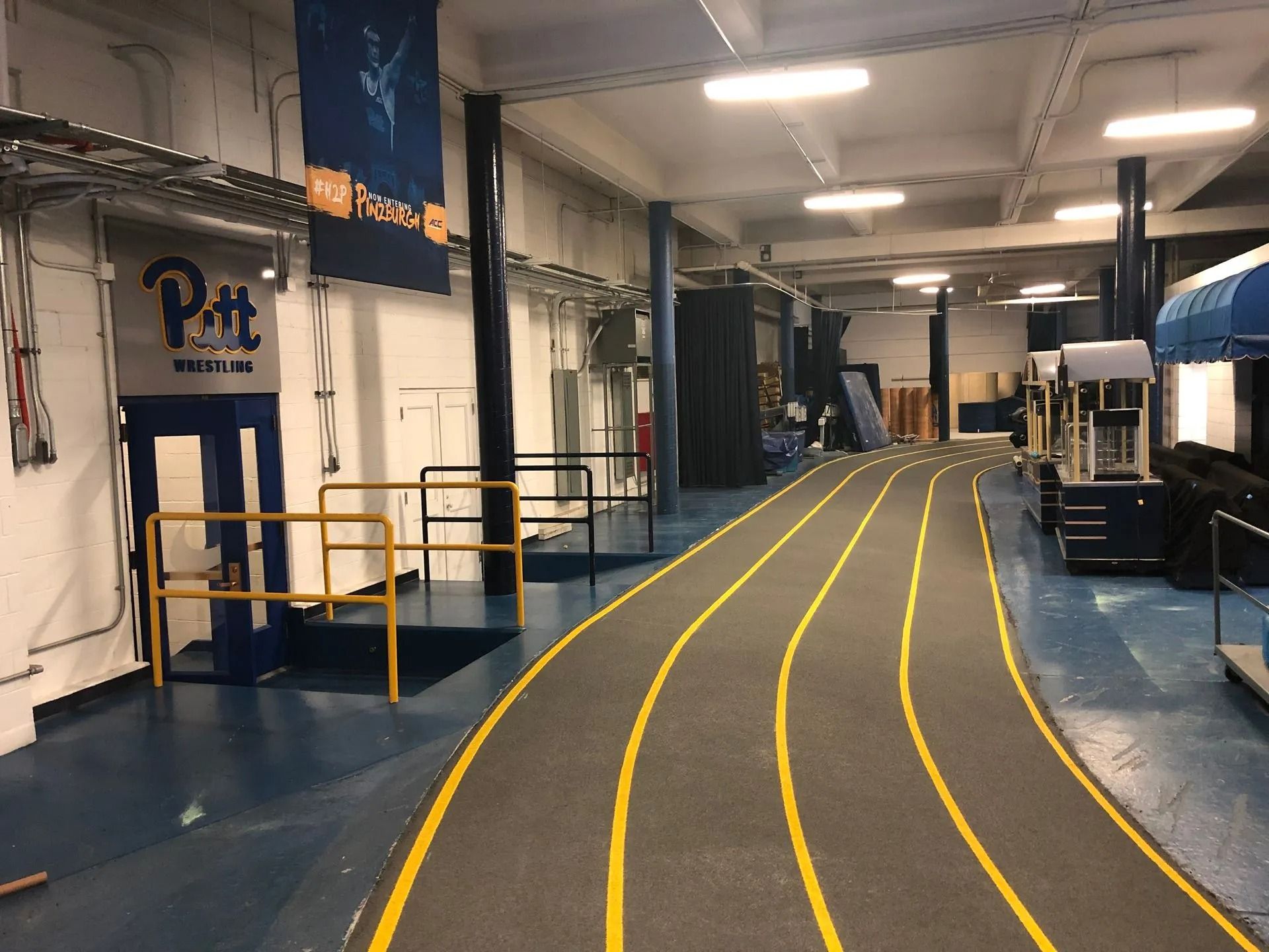 Indoor running track with yellow lane lines, Pitt banners, and equipment.
