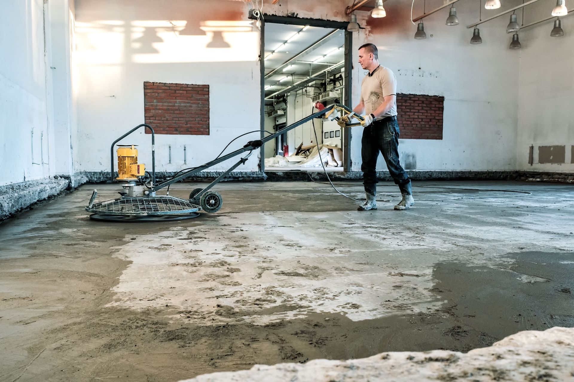 Man using a floor grinder in a large room with a concrete floor.