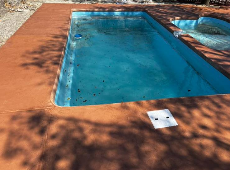 Pool with blue water and reddish-brown concrete deck. Debris floats on the water.