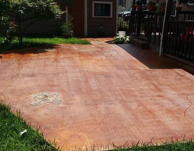 Brown concrete patio with grass edging and small shrubs.