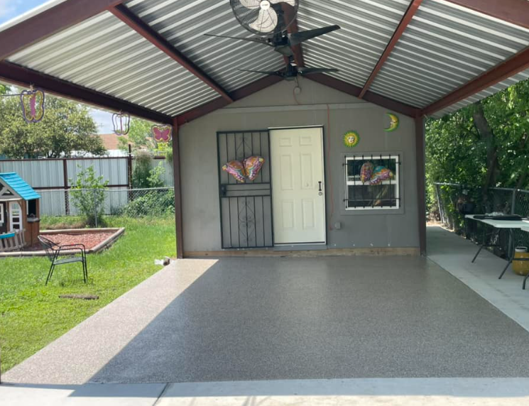 Covered patio with gray epoxy floor, metal roof, and gray building with a white door.