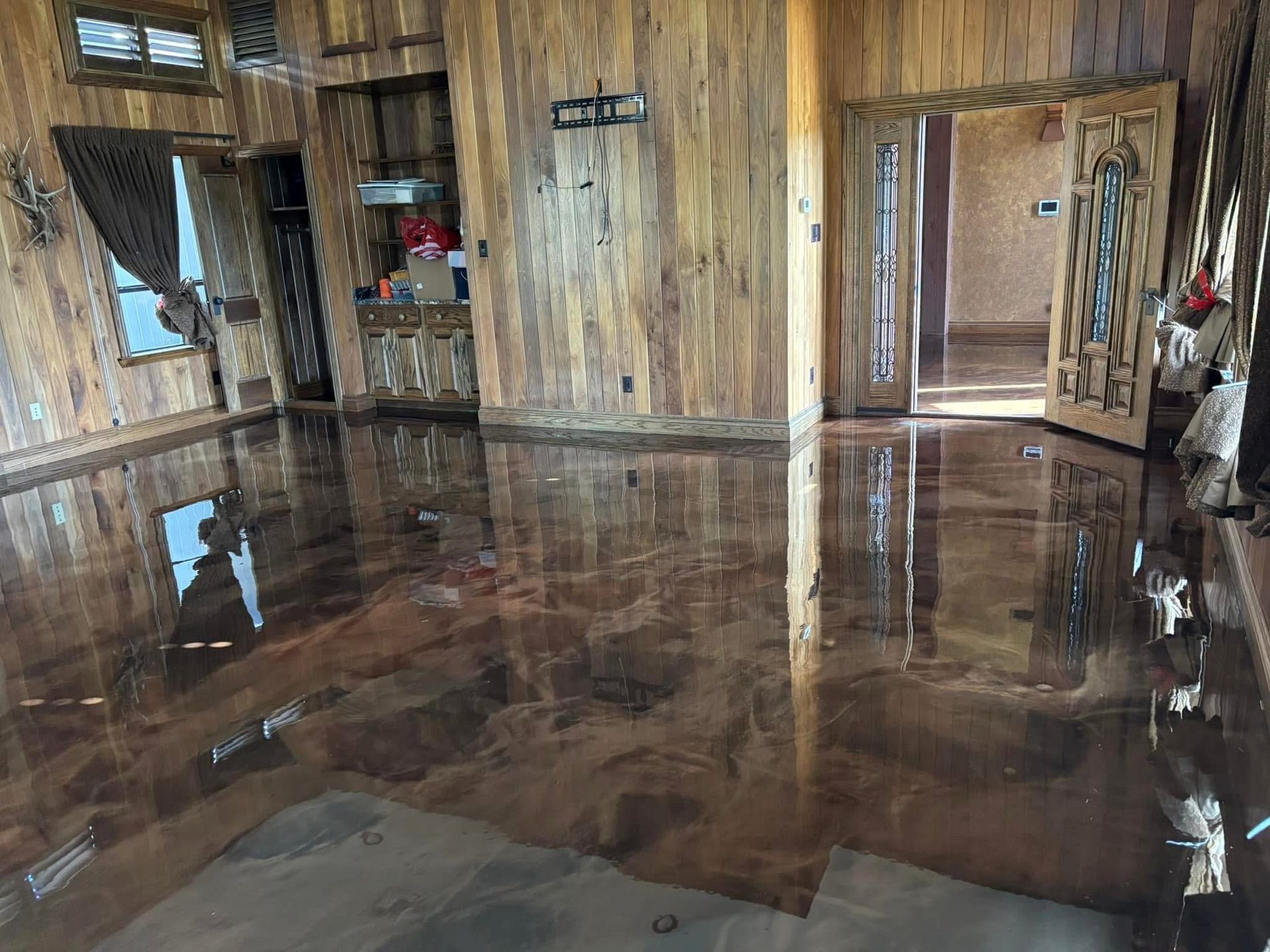 Room with reflective, brown, epoxy flooring, light wooden walls, and open doors.