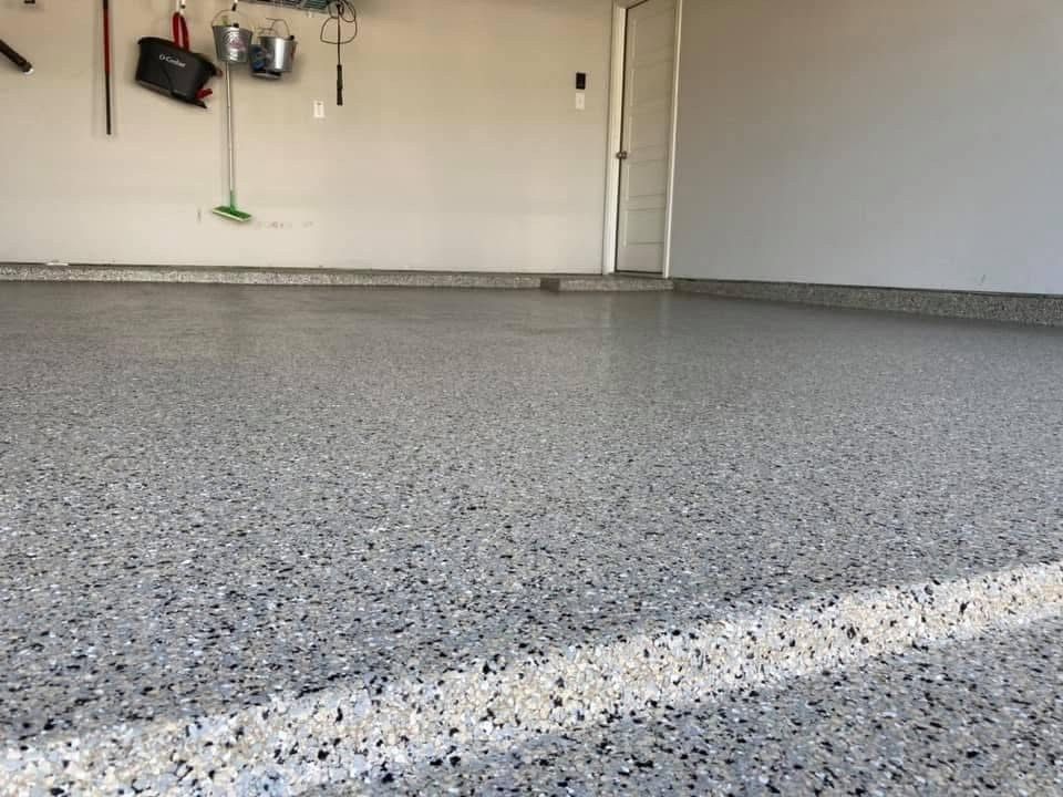 Garage interior with a shiny, speckled epoxy floor and tools hanging on a wall.