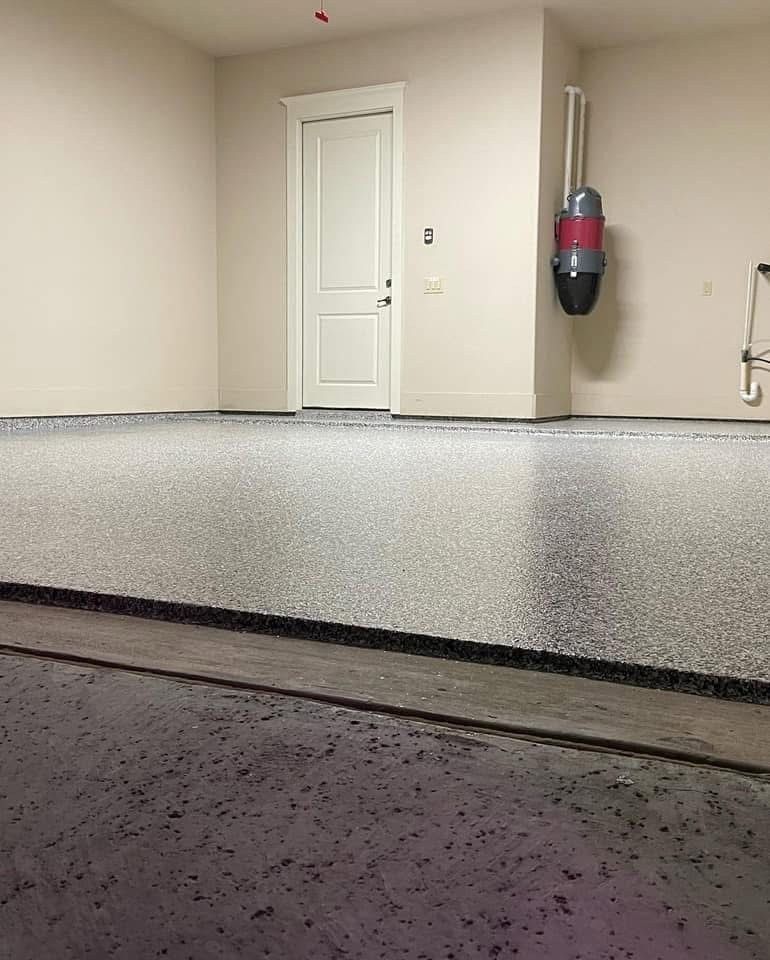 Garage interior with speckled epoxy floor, white walls, closed door, and mounted vacuum.