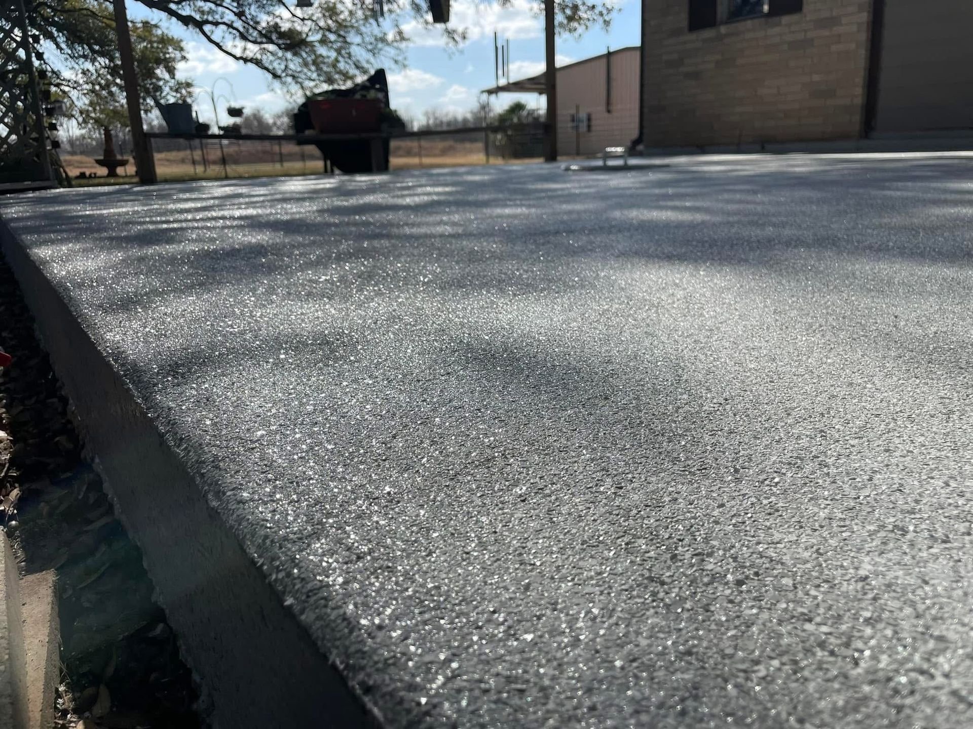 Close-up of a textured, grey concrete surface outdoors with a building and trees in the background under a sunny sky.