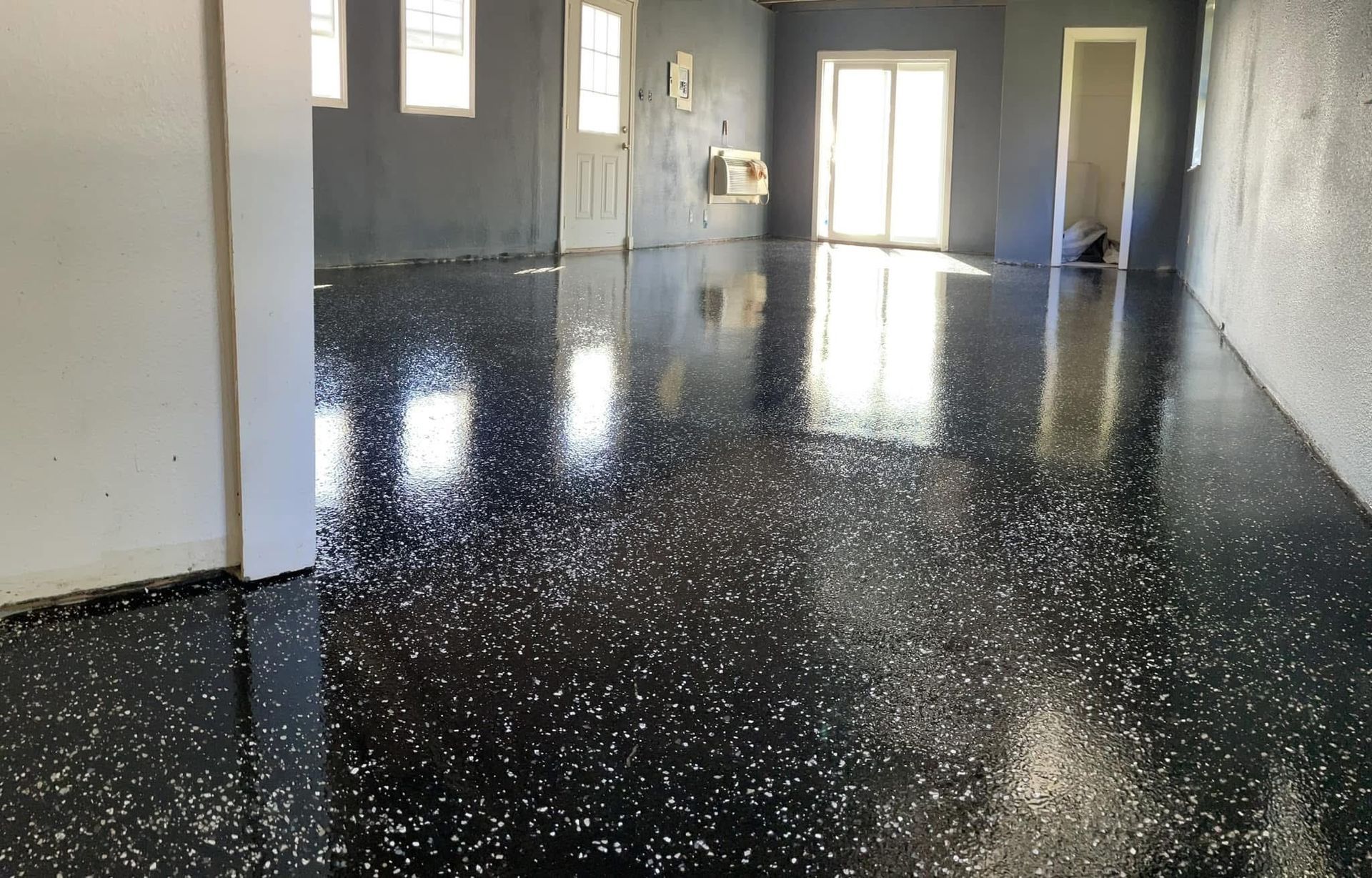 Black and white speckled epoxy floor in a room with white trim, windows, and door.