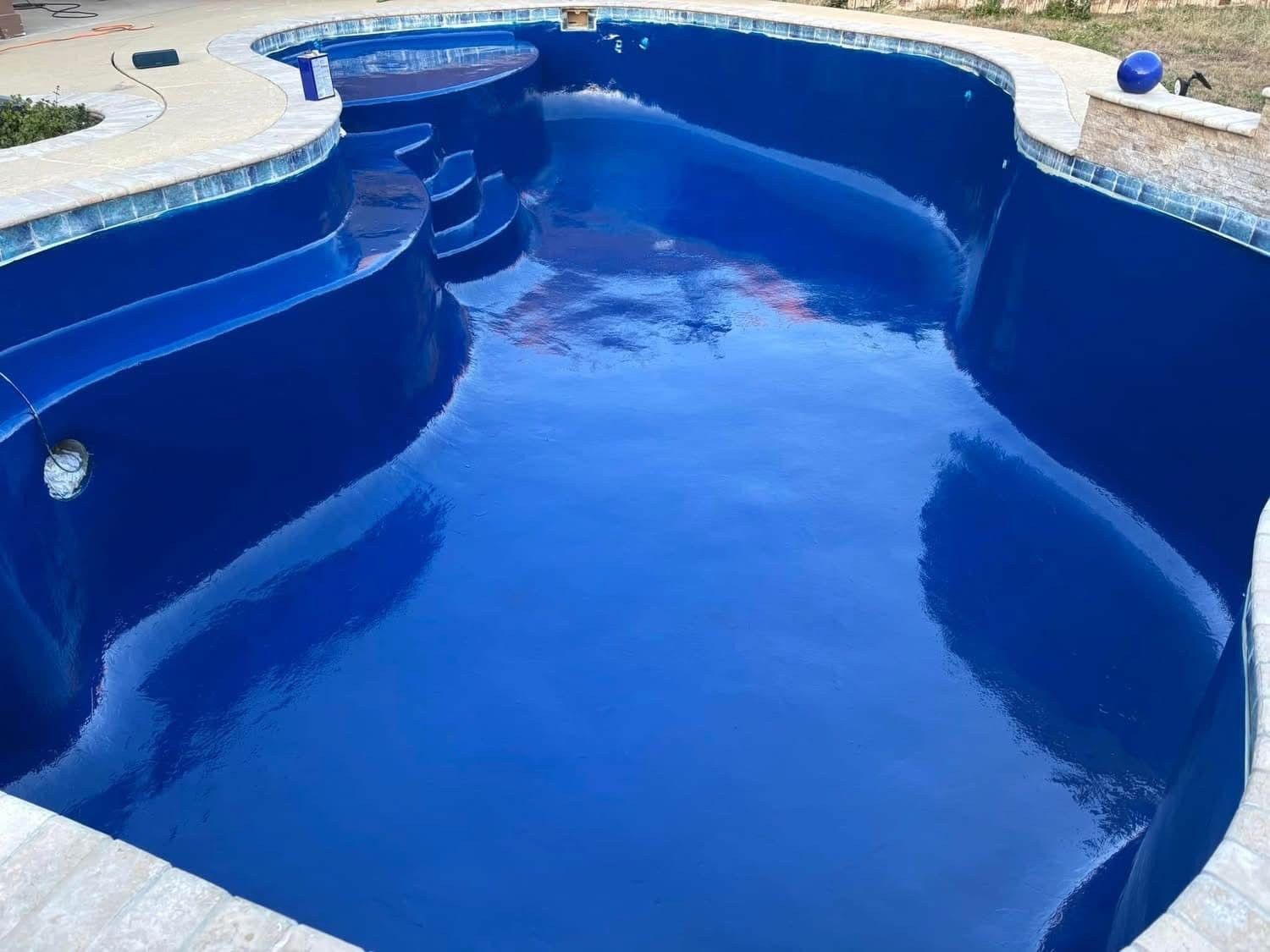 Newly painted blue swimming pool with steps, surrounded by stone coping and mosaic tile.