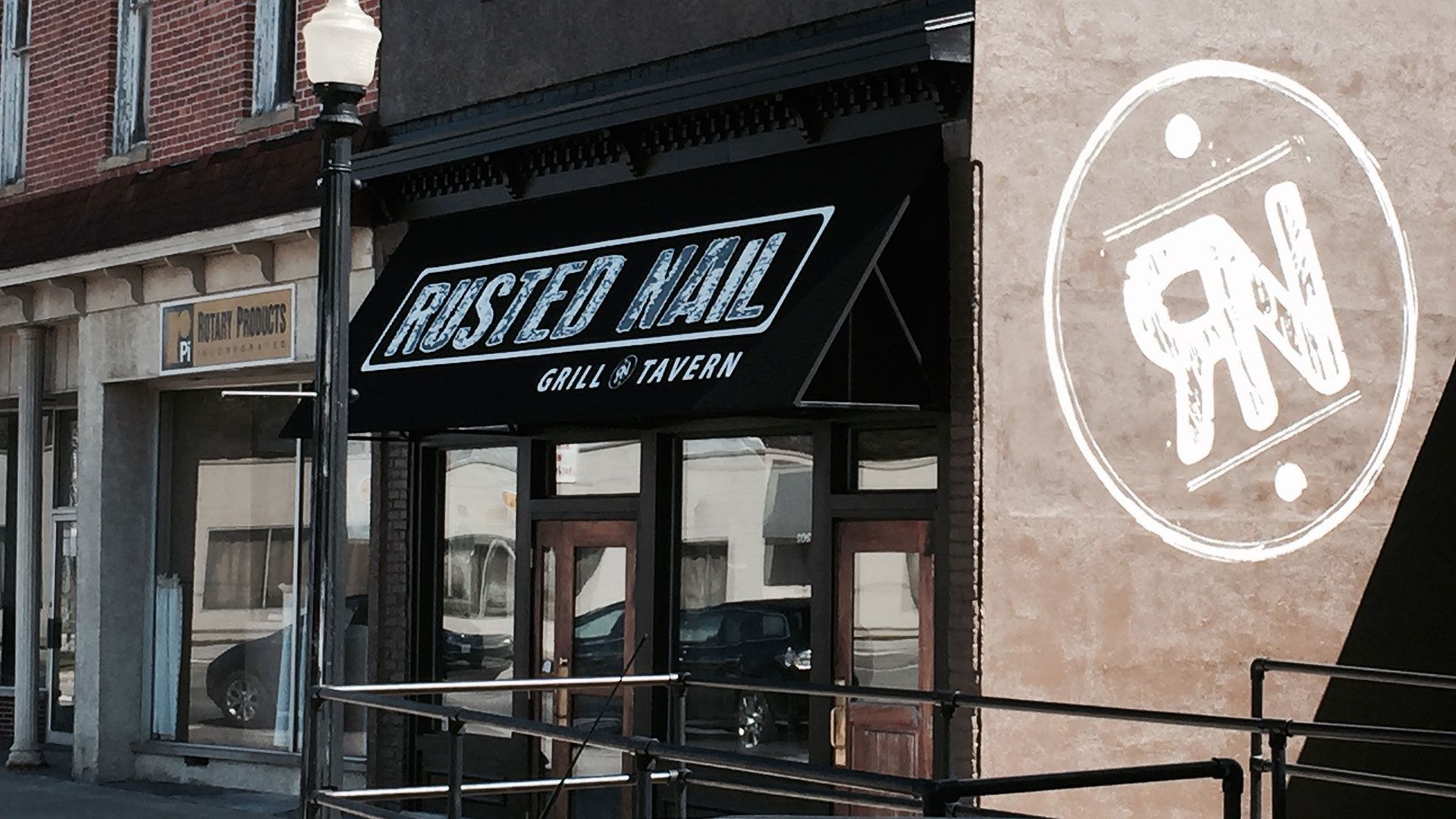 Rusted Nail Grill & Tavern storefront with black awning and logo on building.