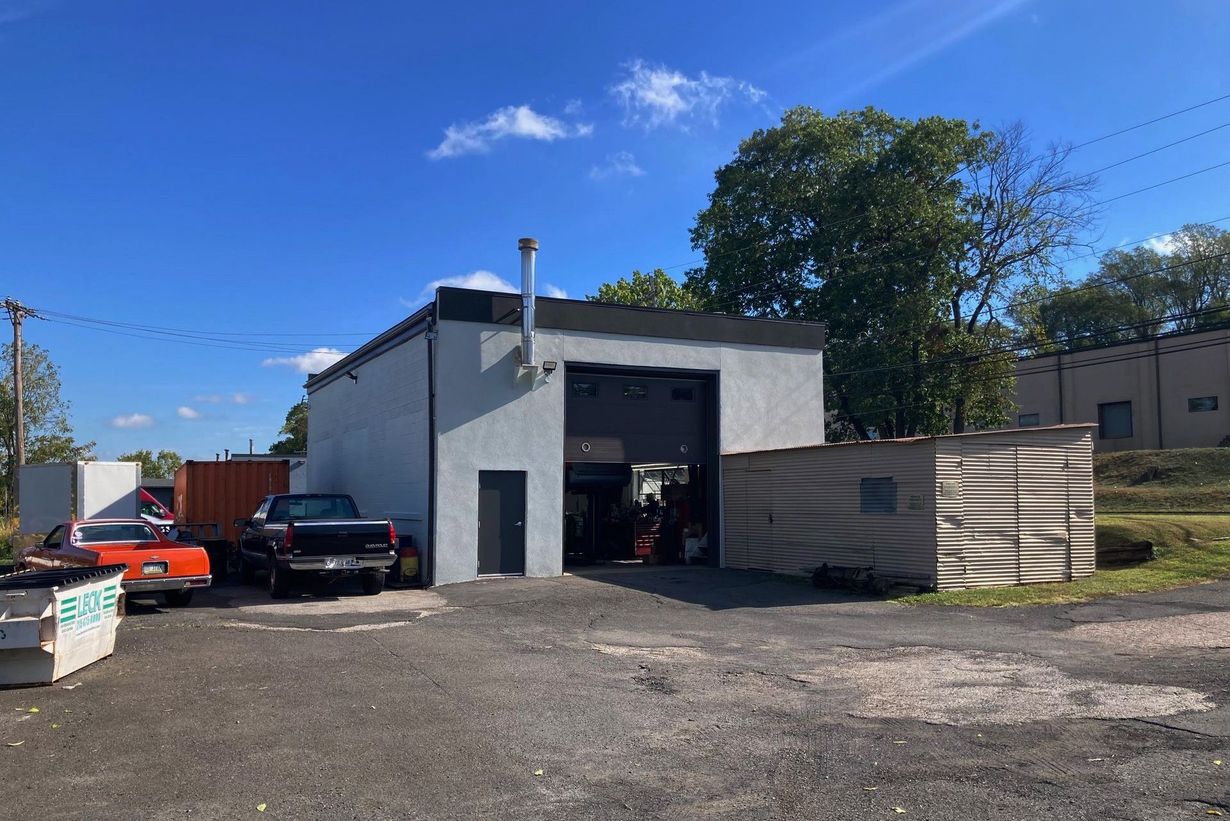 Exterior of a gray commercial building with a large open bay door, vehicles, and a blue sky.