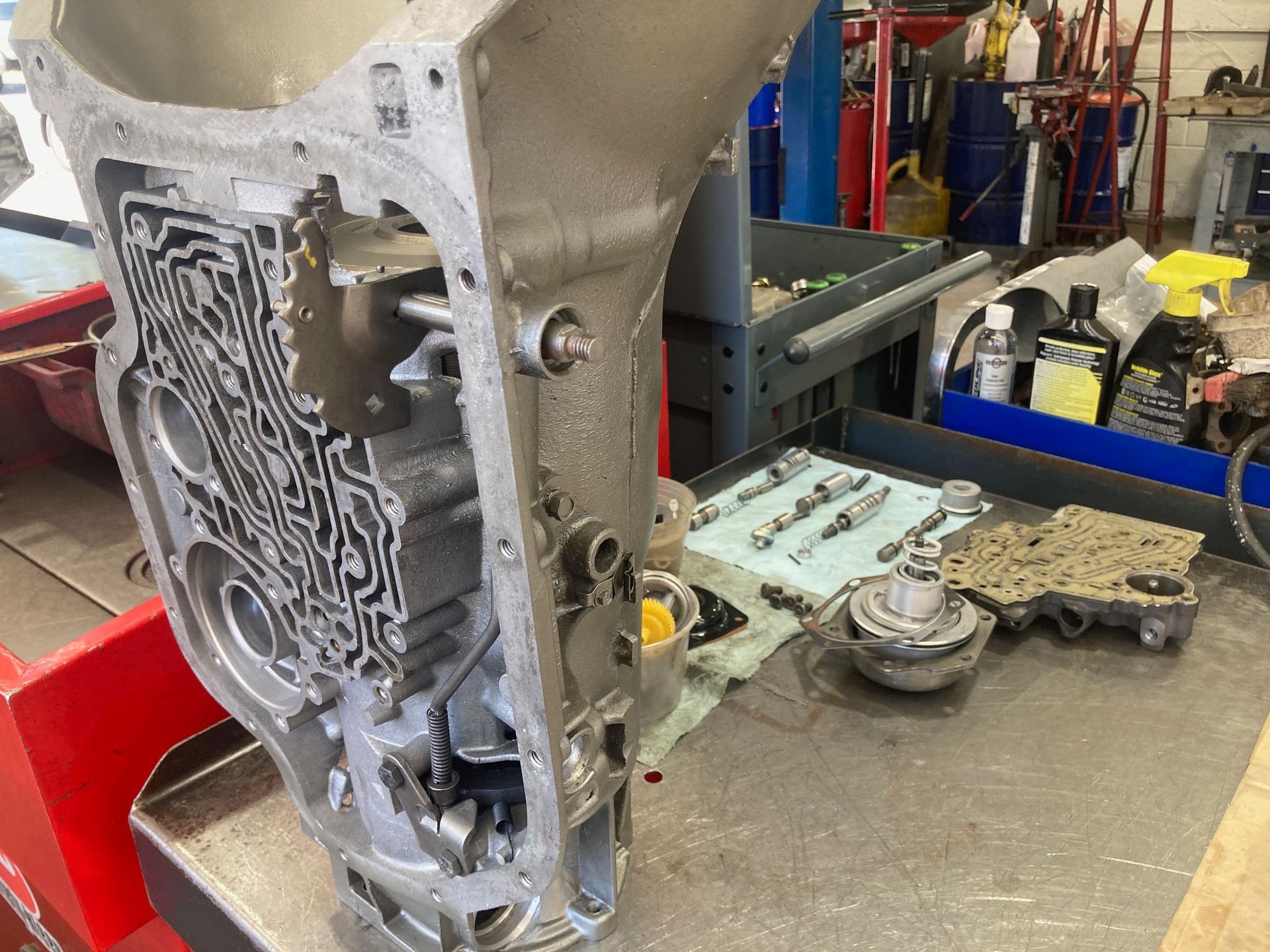 Open the transmission casing on a workbench. Parts and tools are scattered nearby in a repair shop setting.