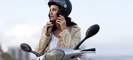 A woman riding a moped with a helmet.