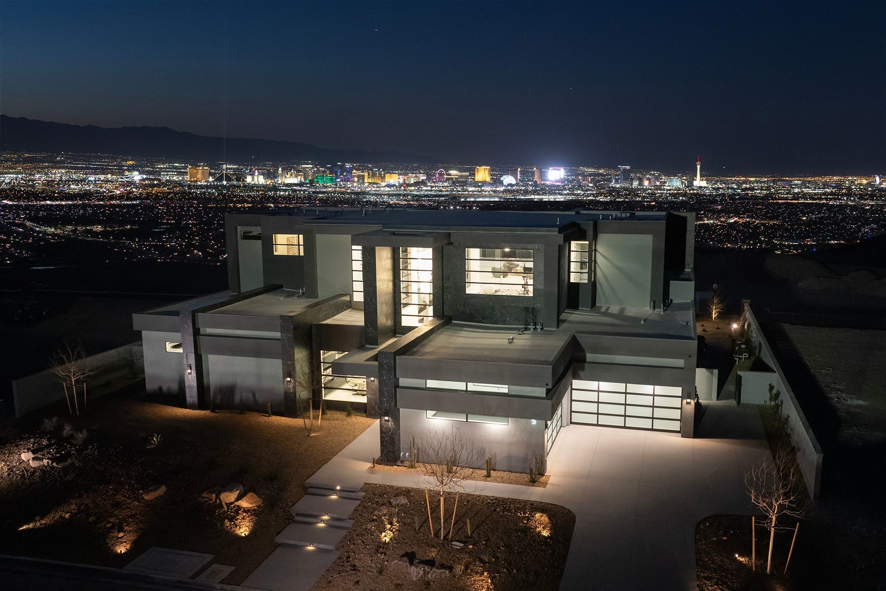 An aerial view of a large house at night with a city in the background.