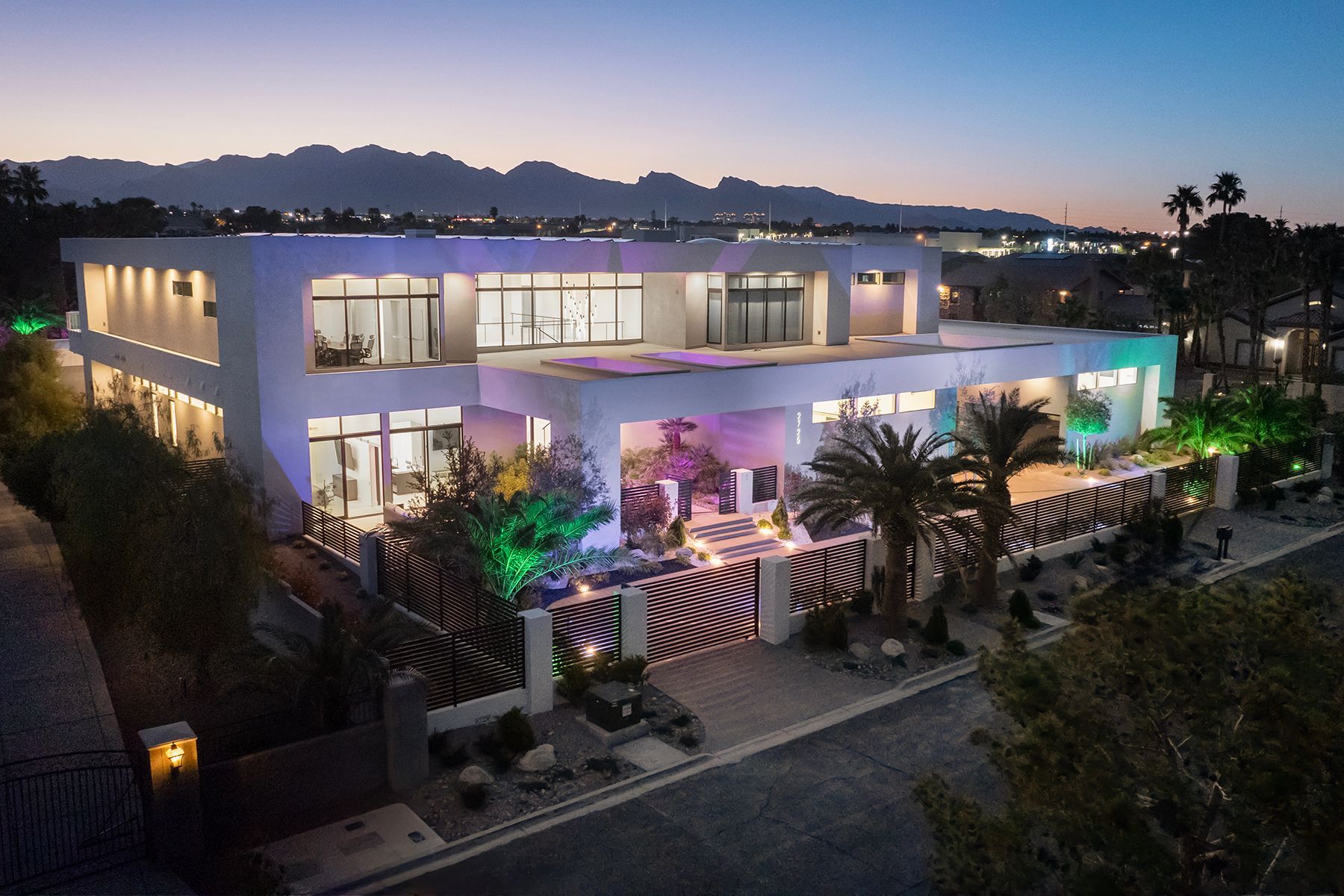 An aerial view of a large white house with palm trees and mountains in the background.