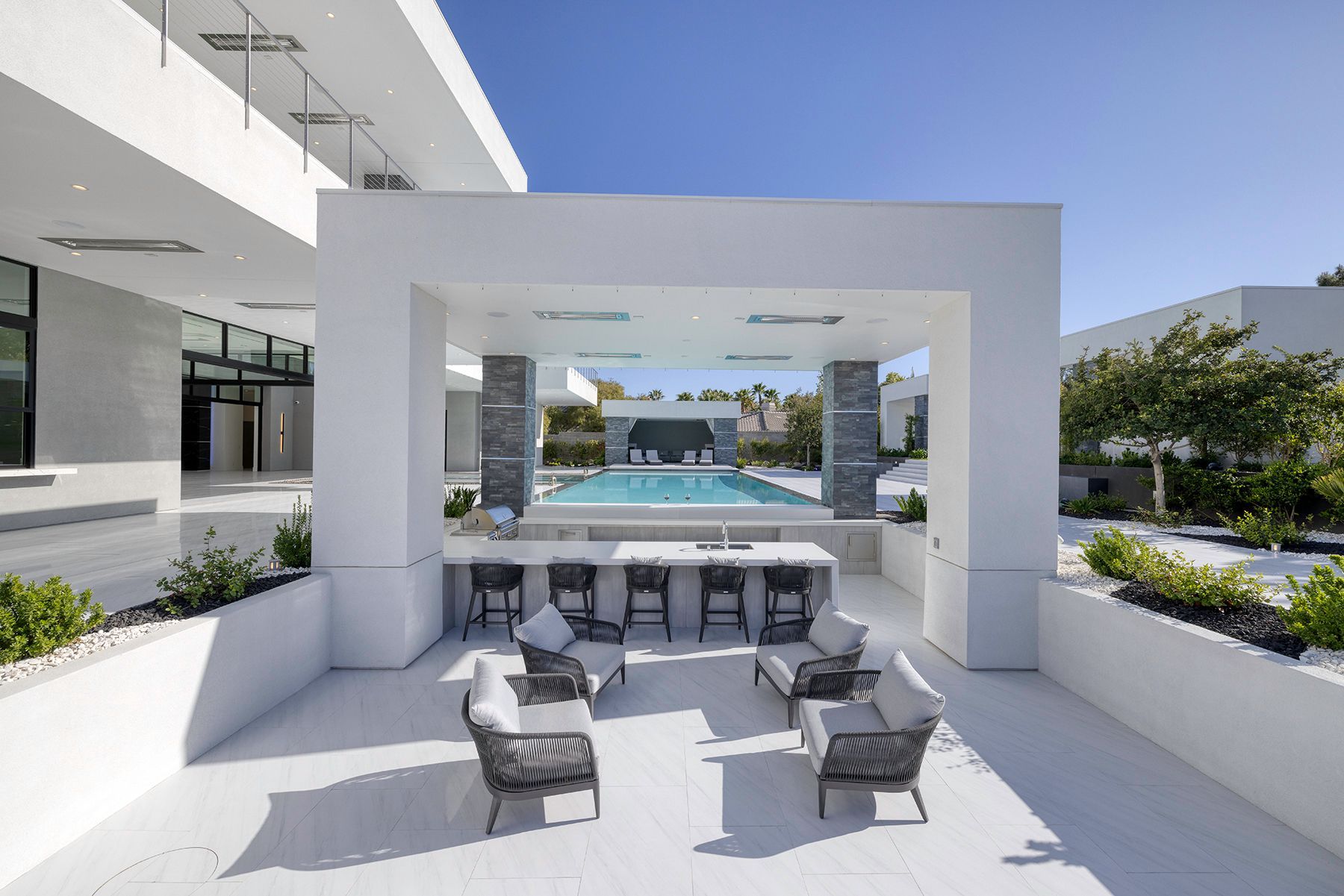A patio with chairs and a table next to a swimming pool.