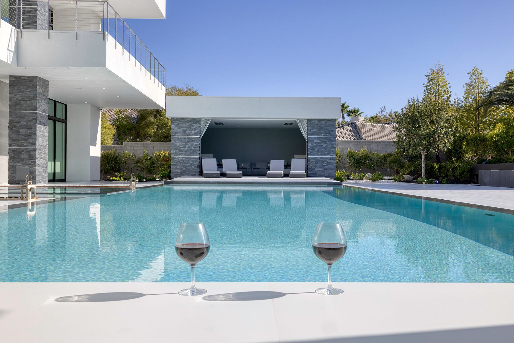 Two glasses of wine are sitting on a table next to a swimming pool.