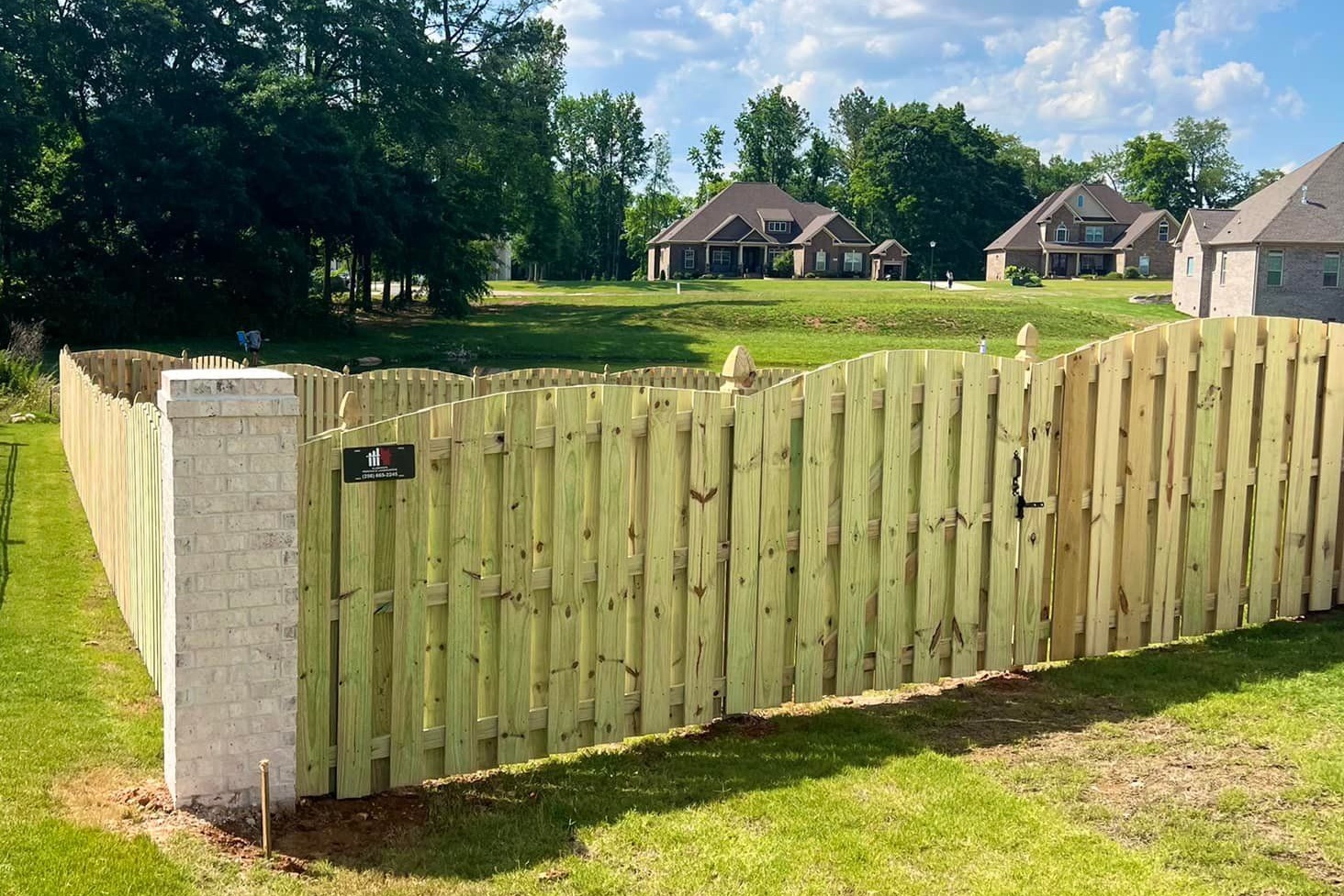 Wooden fence with gate enclosing a grassy area; houses in the background.