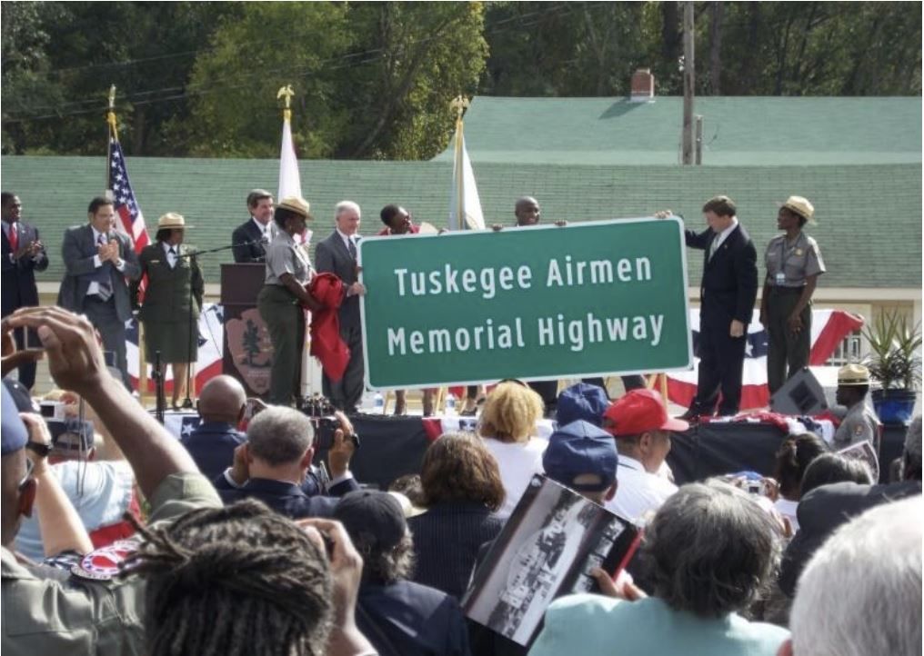 a group of people holding a sign that says tuskegee airmen memorial highway