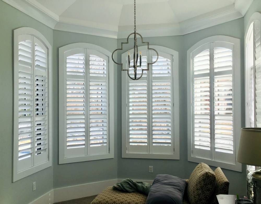 A bedroom with arched windows and white shutters.