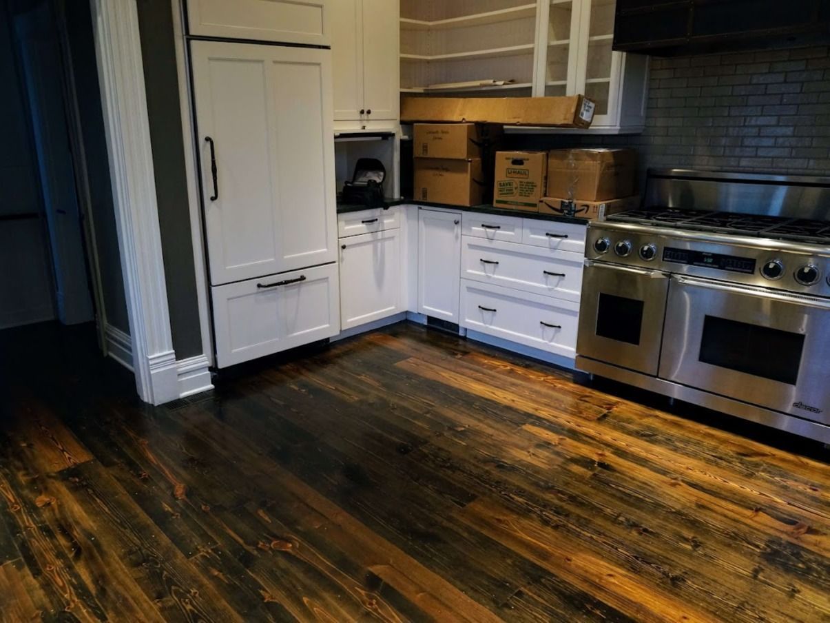 A white kitchen featuring a stainless steel range, custom cabinetry, and dark, rustic stained wood plank flooring.
