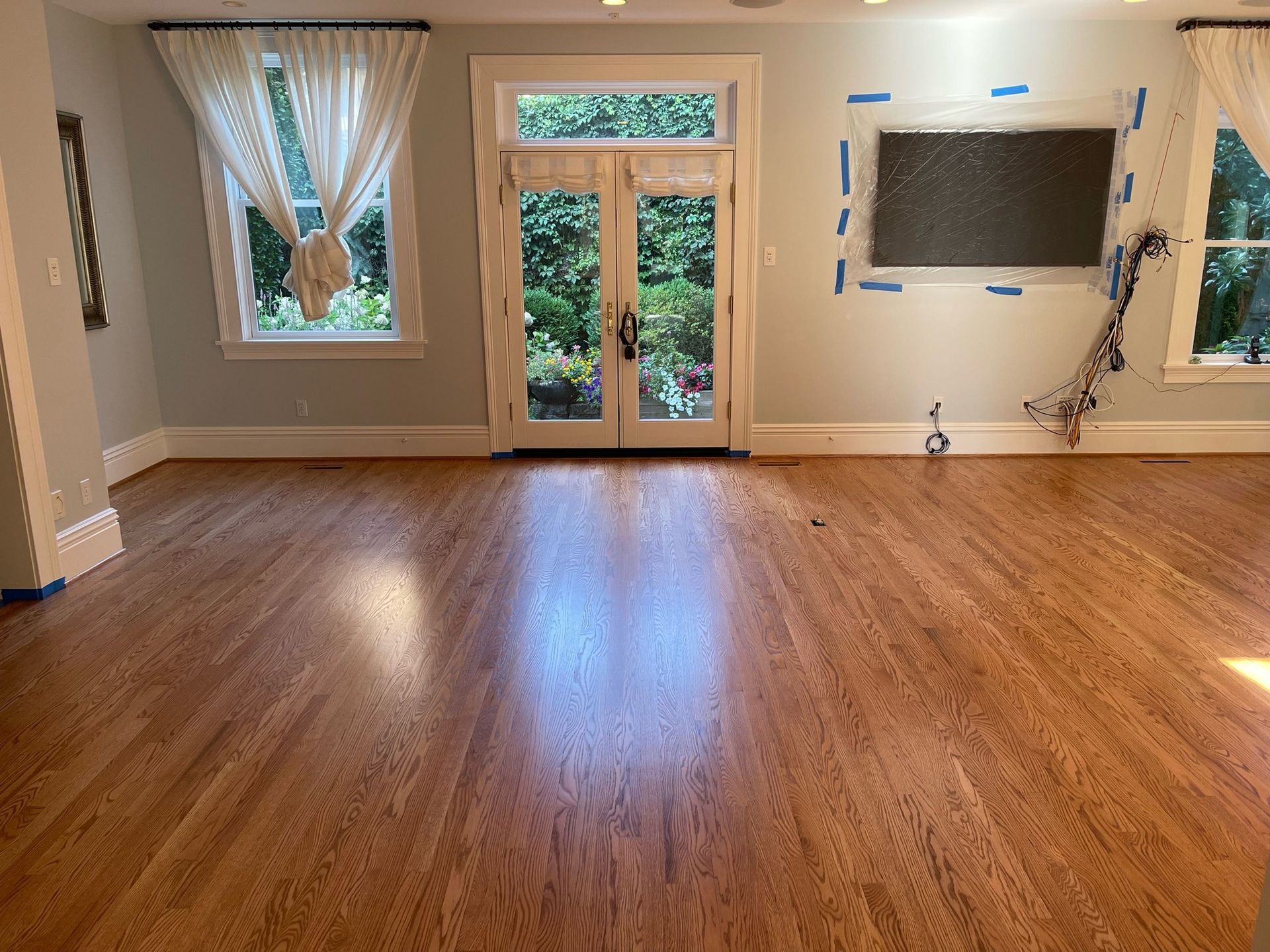 A hardwood-floored room with blue-gray walls, a glass-paneled double door, a window with curtains, and a mounted TV.