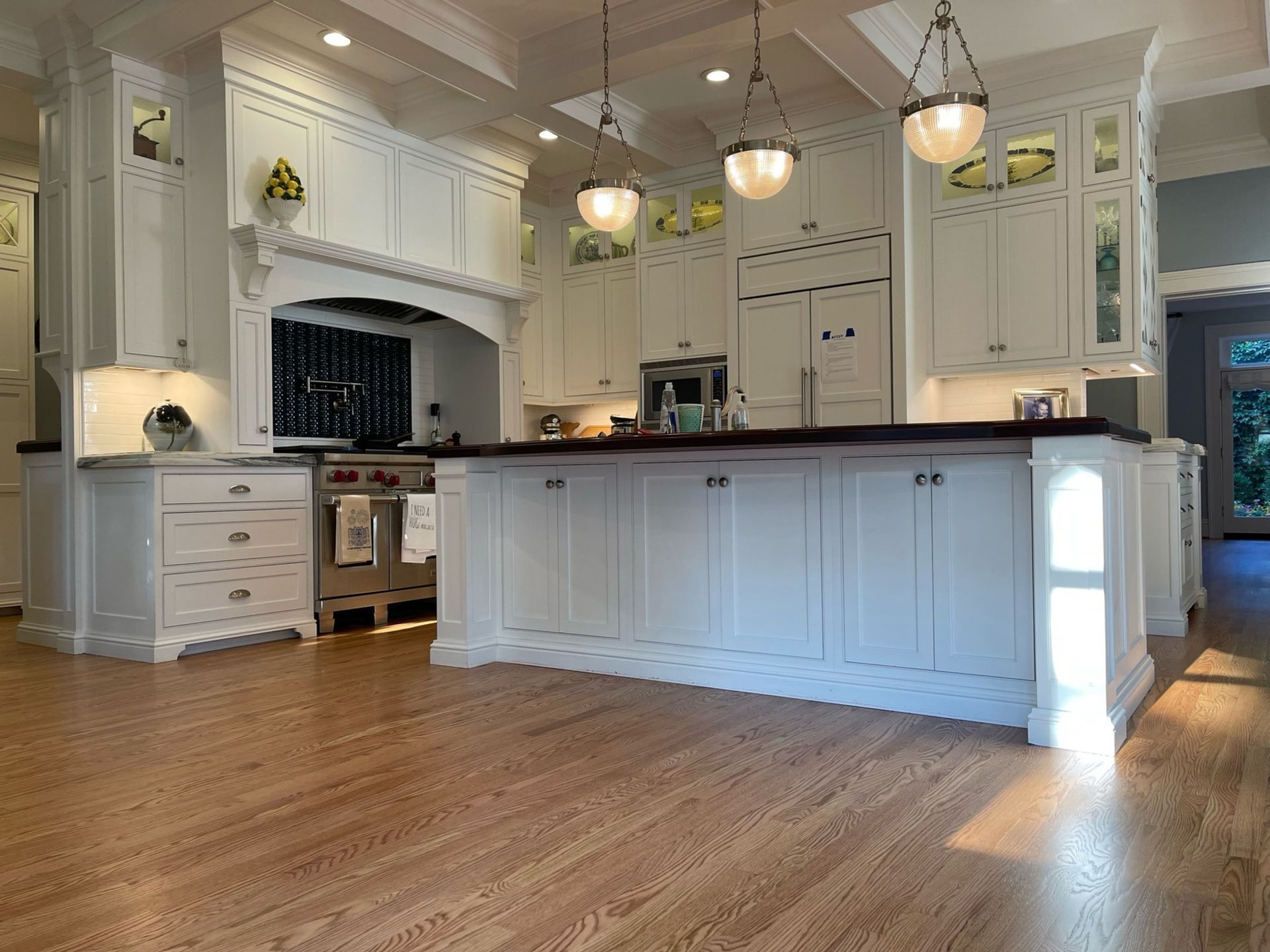 A bright, traditional kitchen with white cabinets, a large central island, stainless steel appliances, and wood flooring.