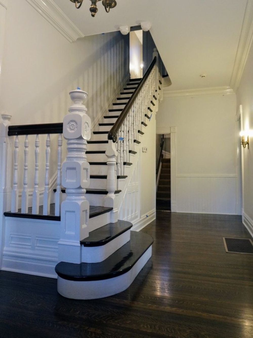 An interior view of a home entrance featuring a grand white staircase with dark treads and a polished wooden floor.