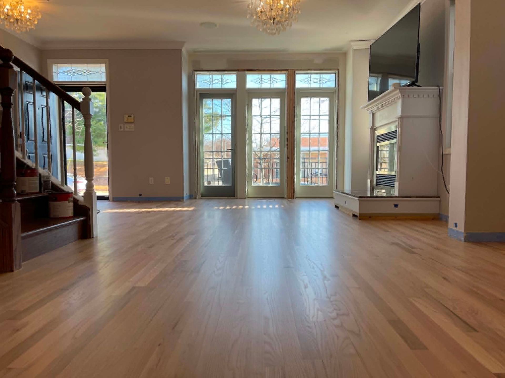 Empty living room with hardwood floors, chandelier, and glass doors opening to a balcony.