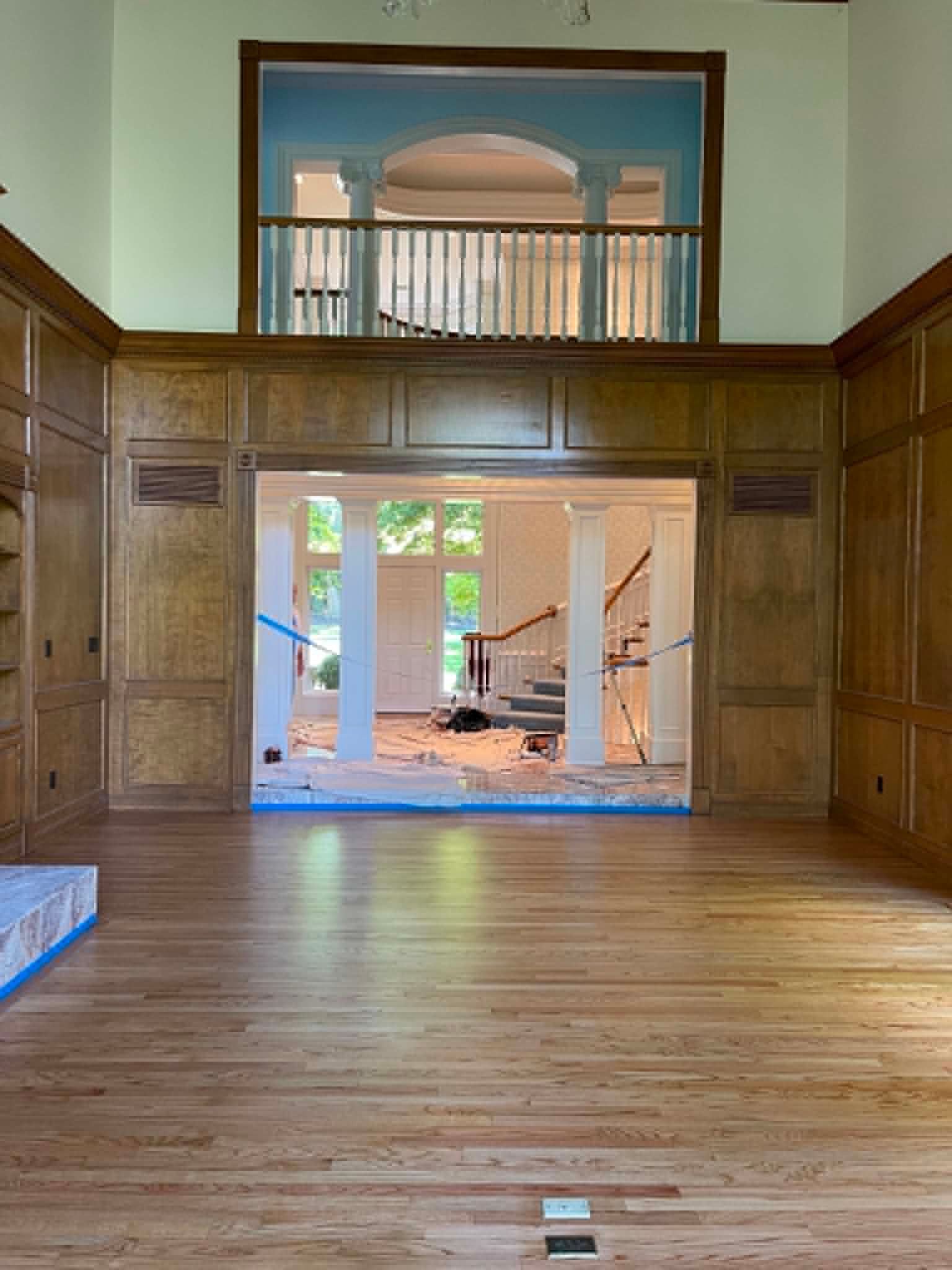 Wood-paneled room opening to a bright porch through large glass doors, with an upper balcony above.