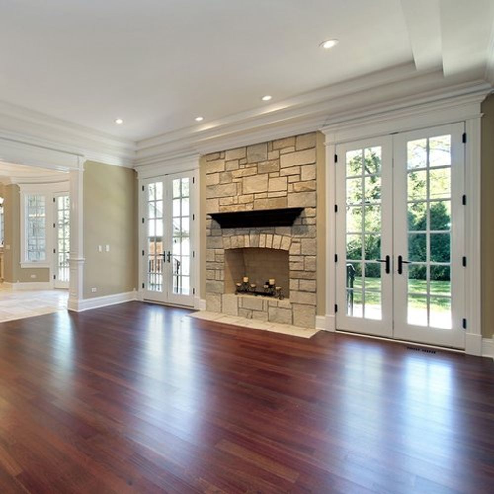 An elegant living room with dark hardwood floors, a stone fireplace, and double French doors opening to a garden.