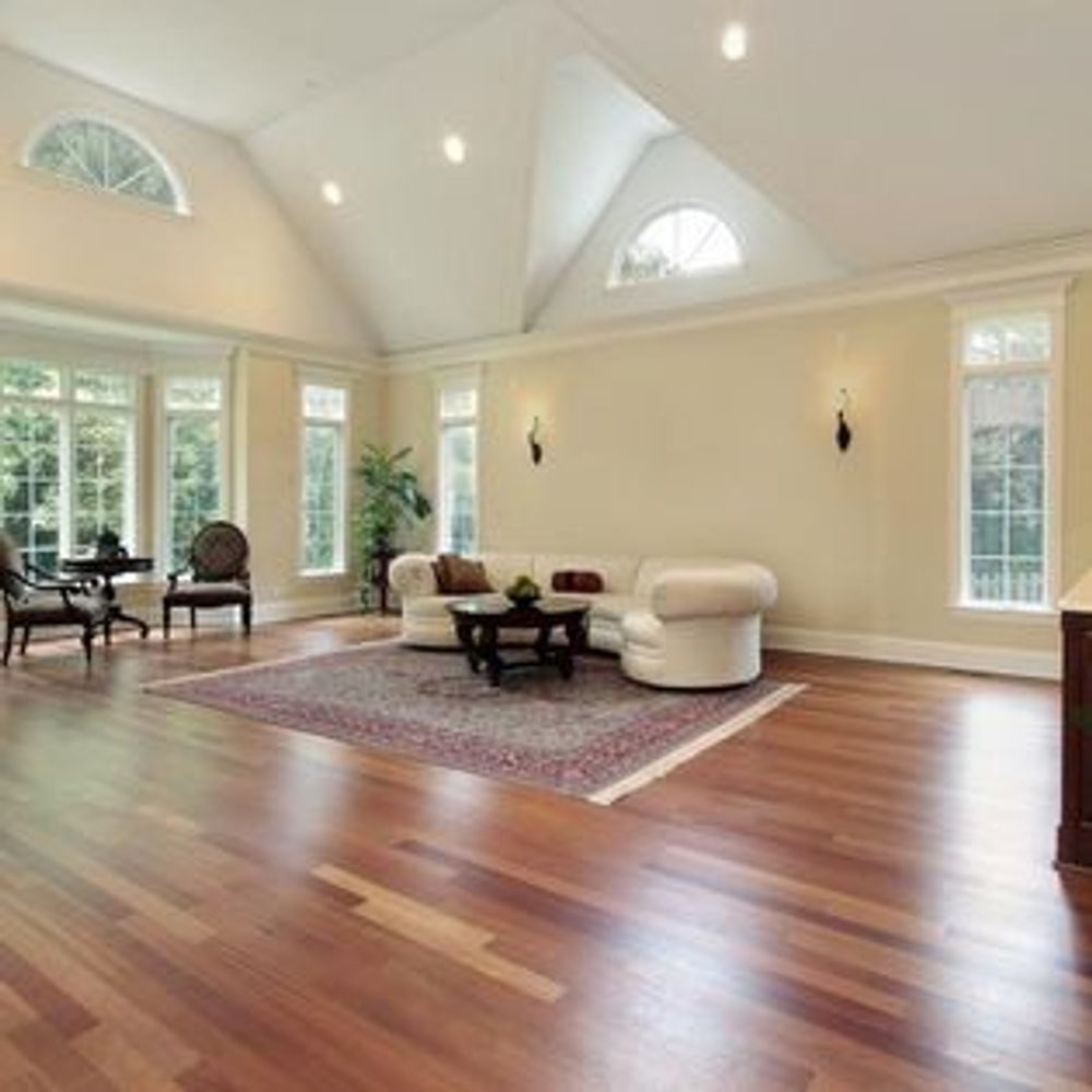 A spacious living room with cream walls, hardwood floors, a white sectional, a dark coffee table, and large windows.