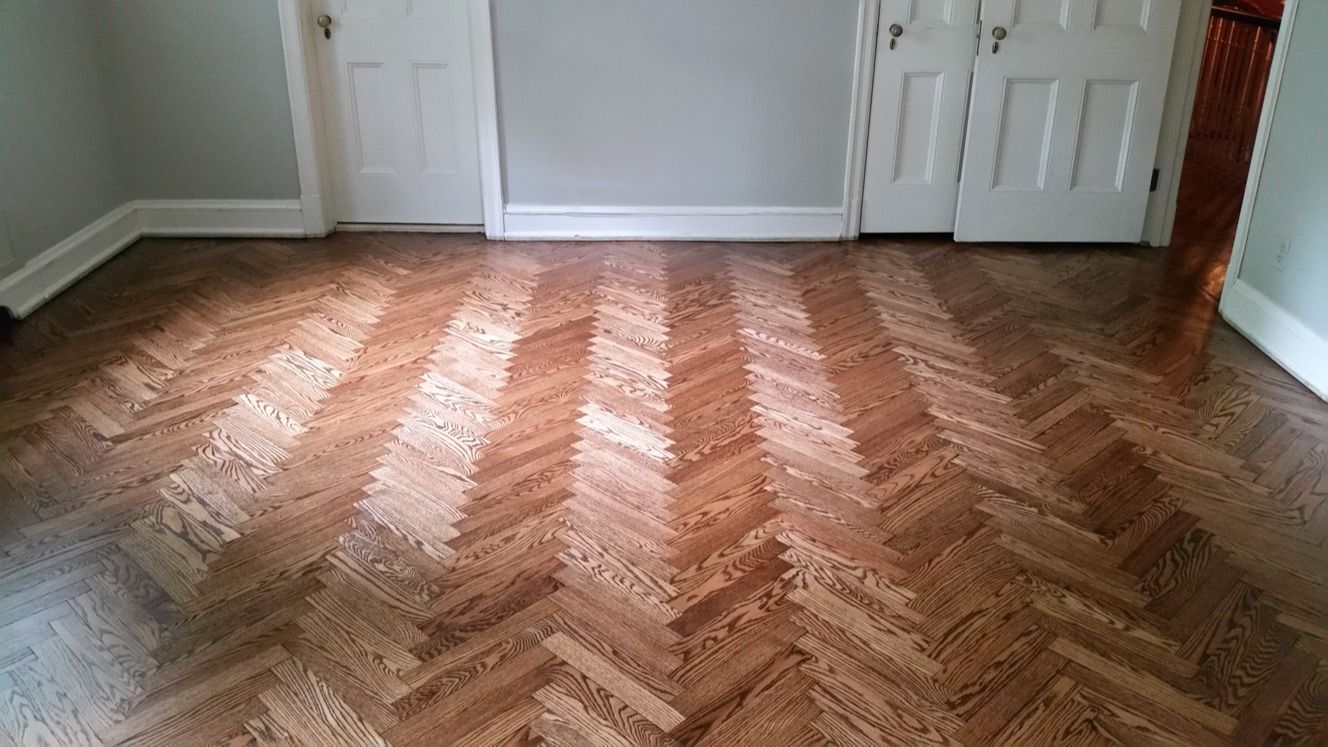 A room featuring a light and dark brown herringbone wood floor pattern with white walls and closed white doors.