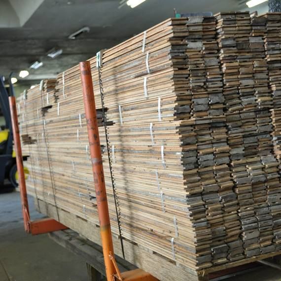 A large, neatly stacked pile of long wooden planks resting on a metal flatbed trolley inside a warehouse.
