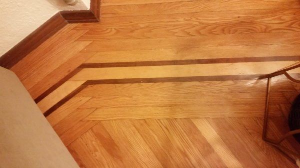 A light-colored hardwood floor featuring a diagonal herringbone pattern with a dark wood transition strip across the middle.
