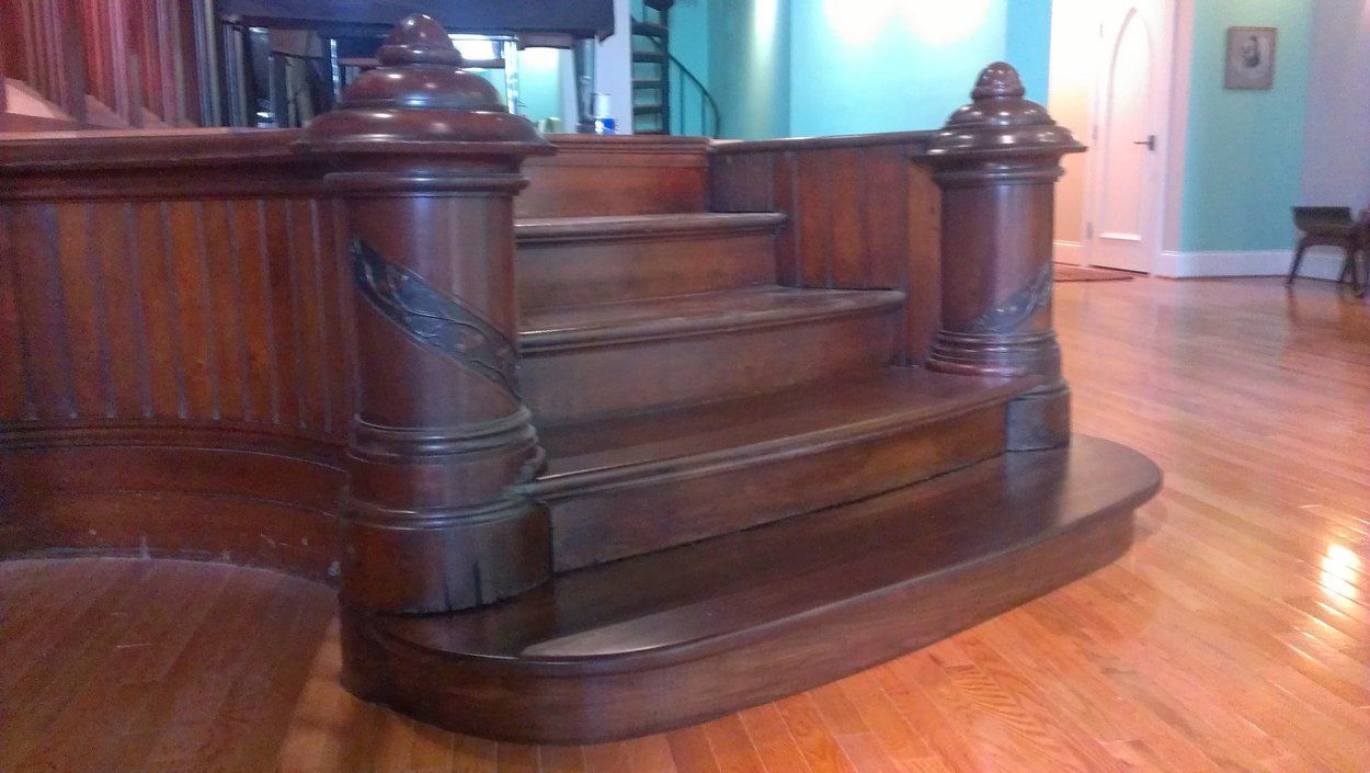 A set of two wide, polished wooden steps with decorative, carved pillars on either side, set within a spacious room.
