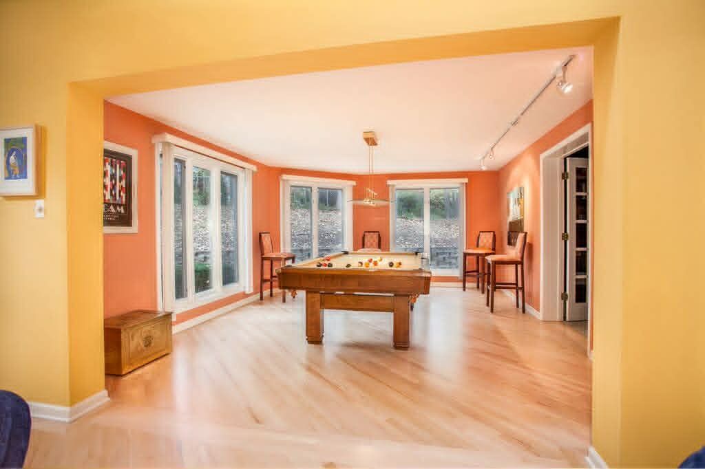 Bright game room with a pool table, large windows, and orange walls with wood flooring.